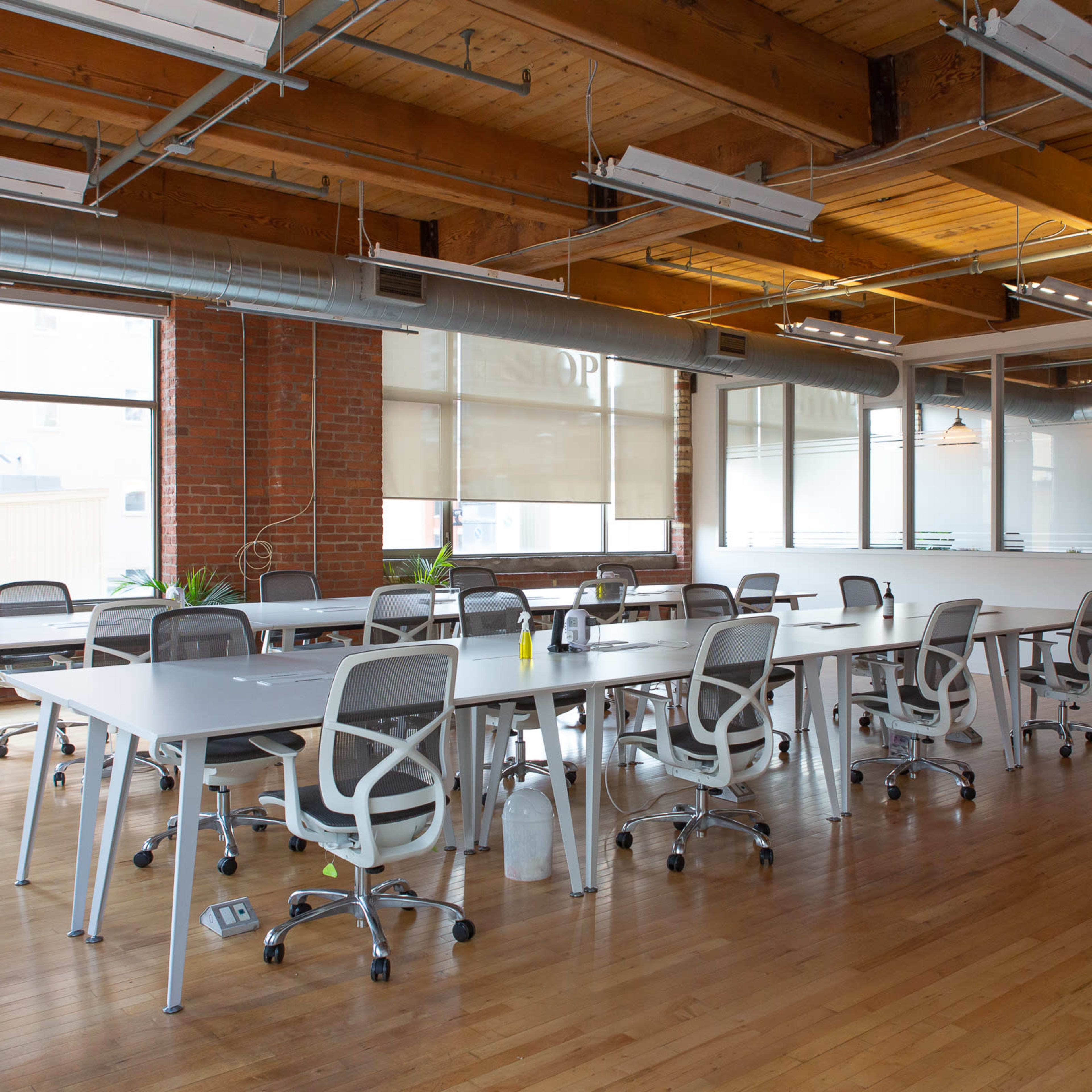 A modern office space with wooden floors, large windows, and several rows of desks with ergonomic chairs.
