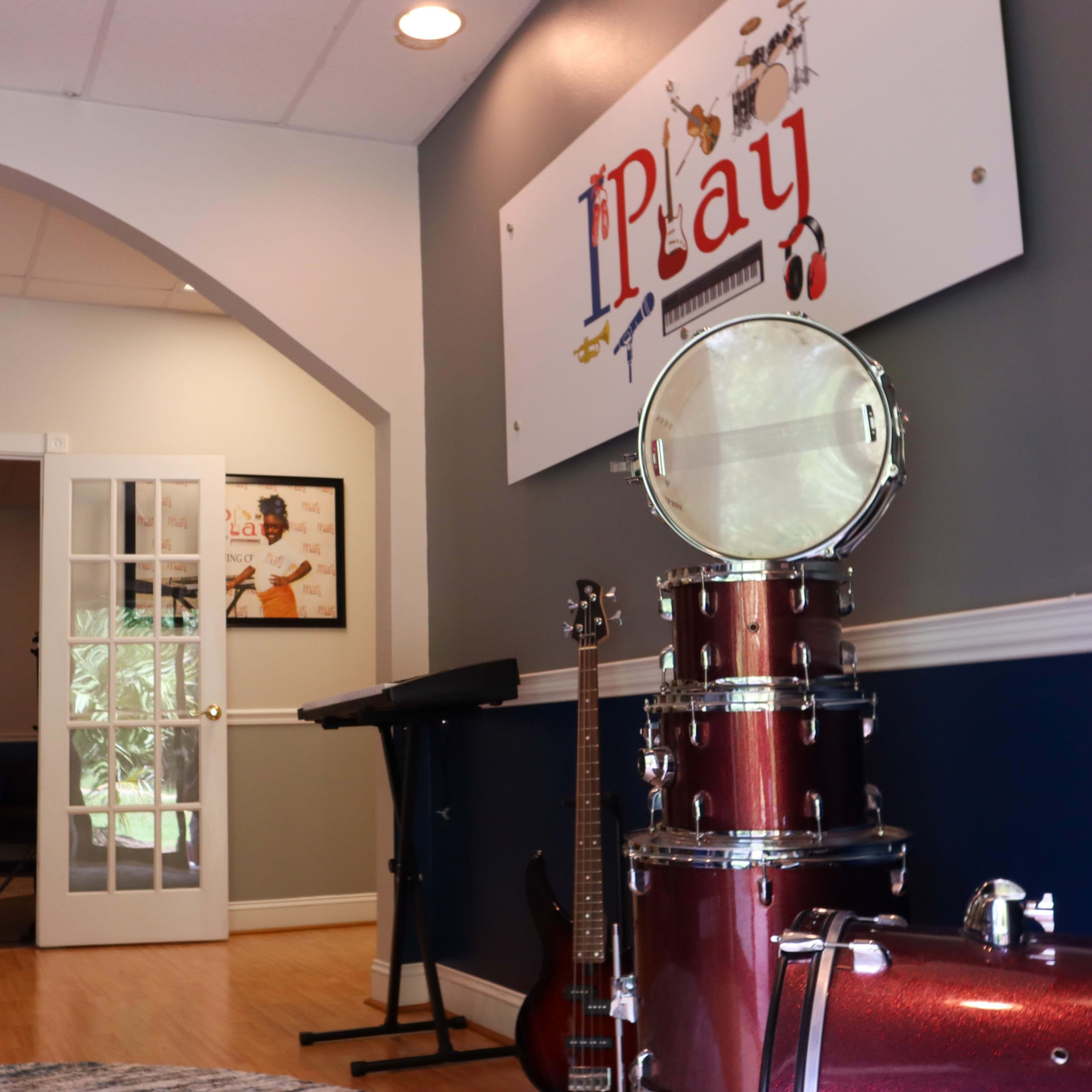 An interior space with musical instruments, including a drum set and guitar, and a sign that reads "iPlay" on the wall.