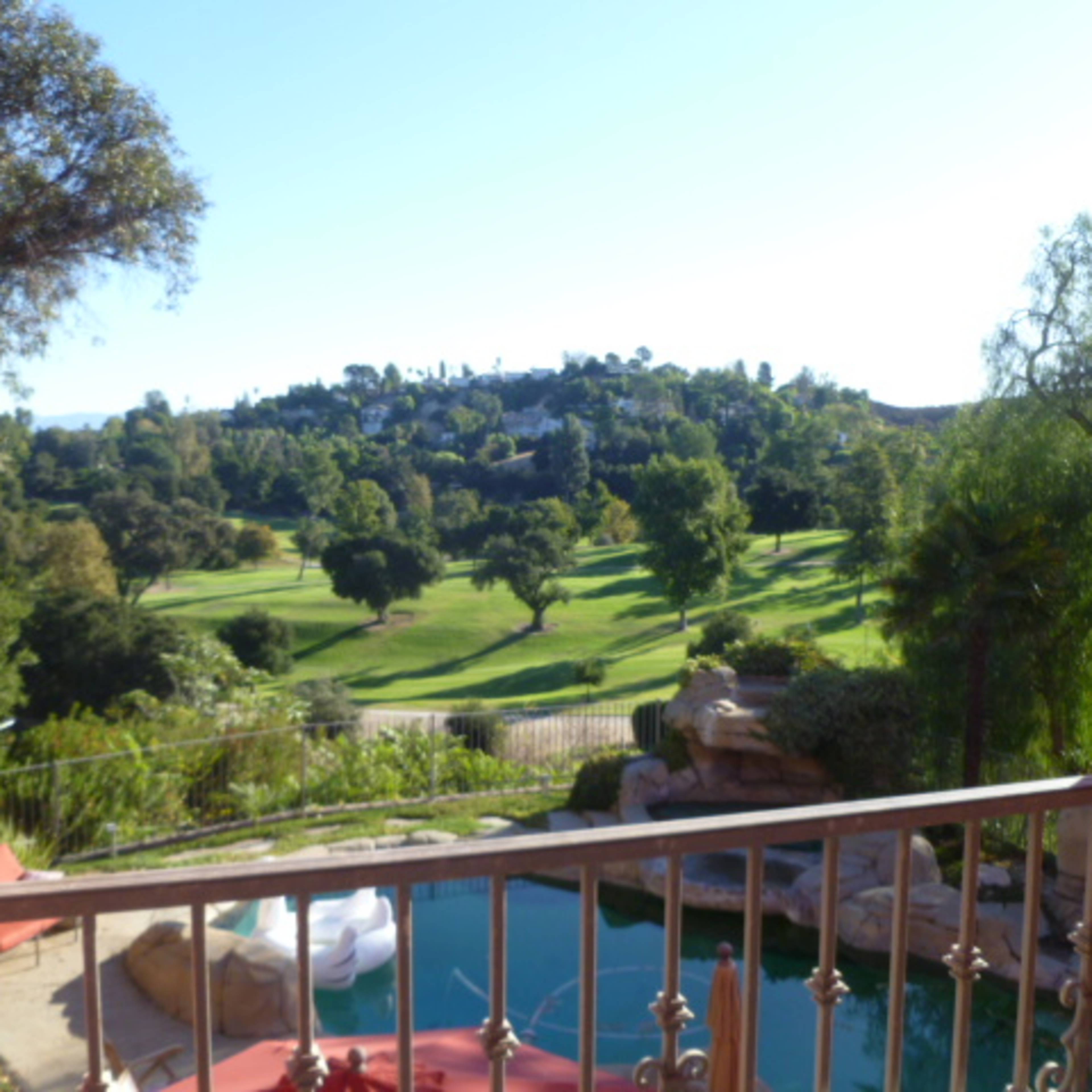 A view of a green golf course and hills is seen from a balcony with a swimming pool in the foreground.