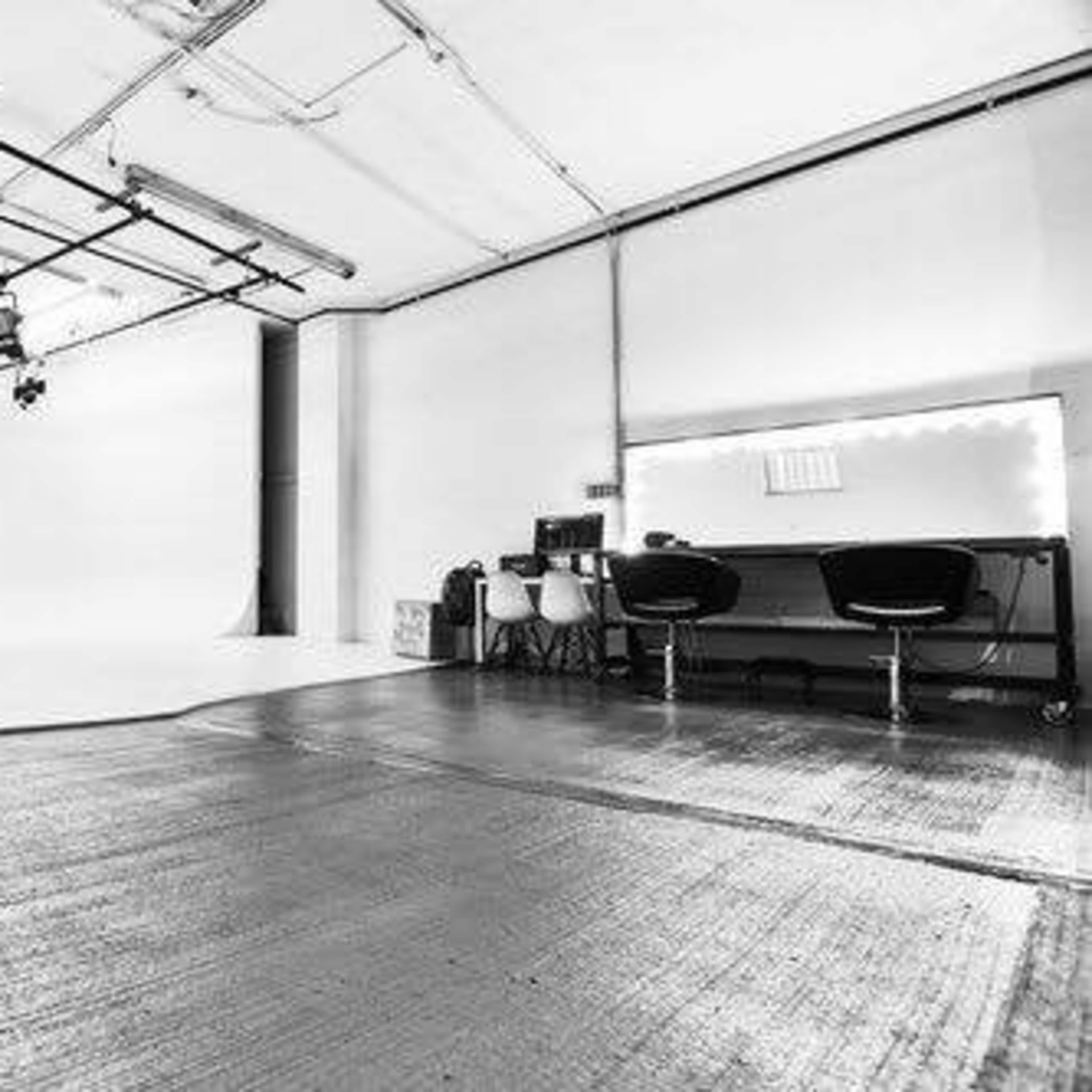 A spacious, empty photography studio with lights mounted on a grid and a mirrored vanity area along one wall.