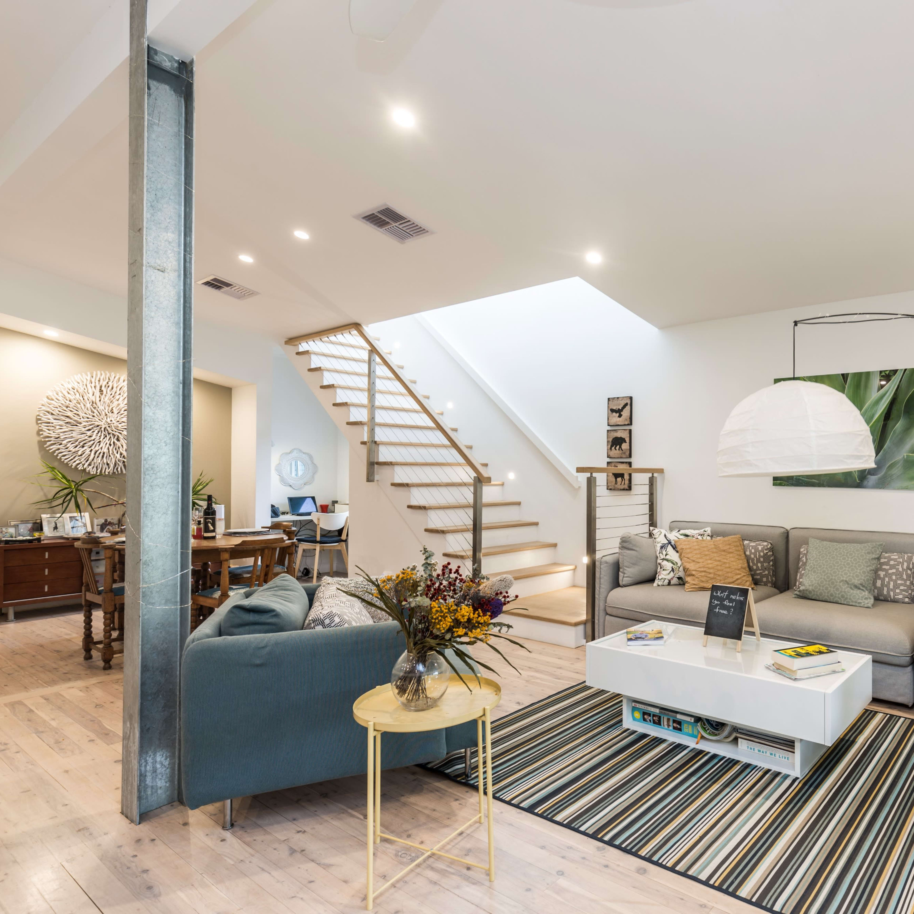 A modern living room with a gray sectional couch, a round coffee table, a striped rug, and a staircase leading to an upper level.