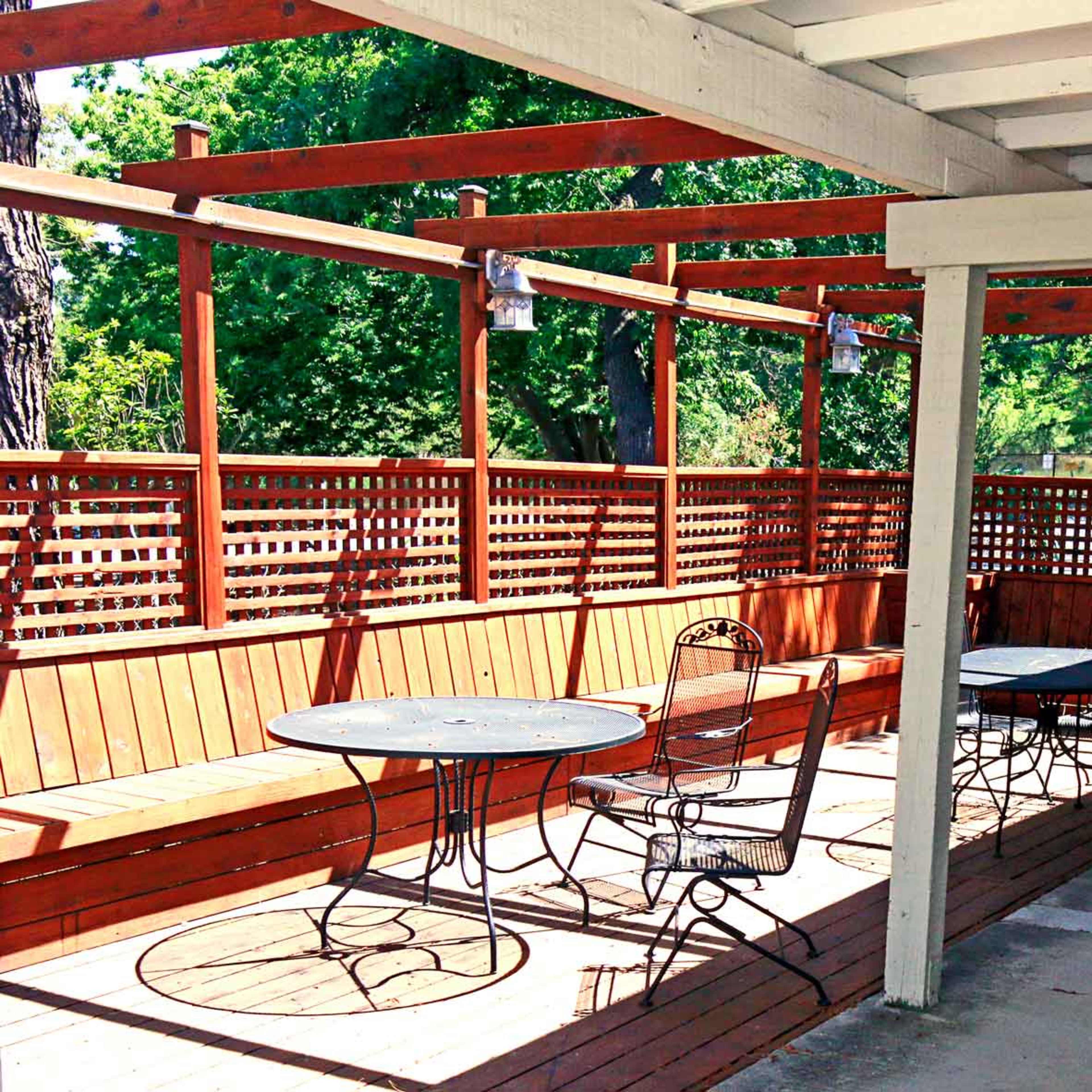 A covered outdoor seating area with wooden benches and round metal tables.