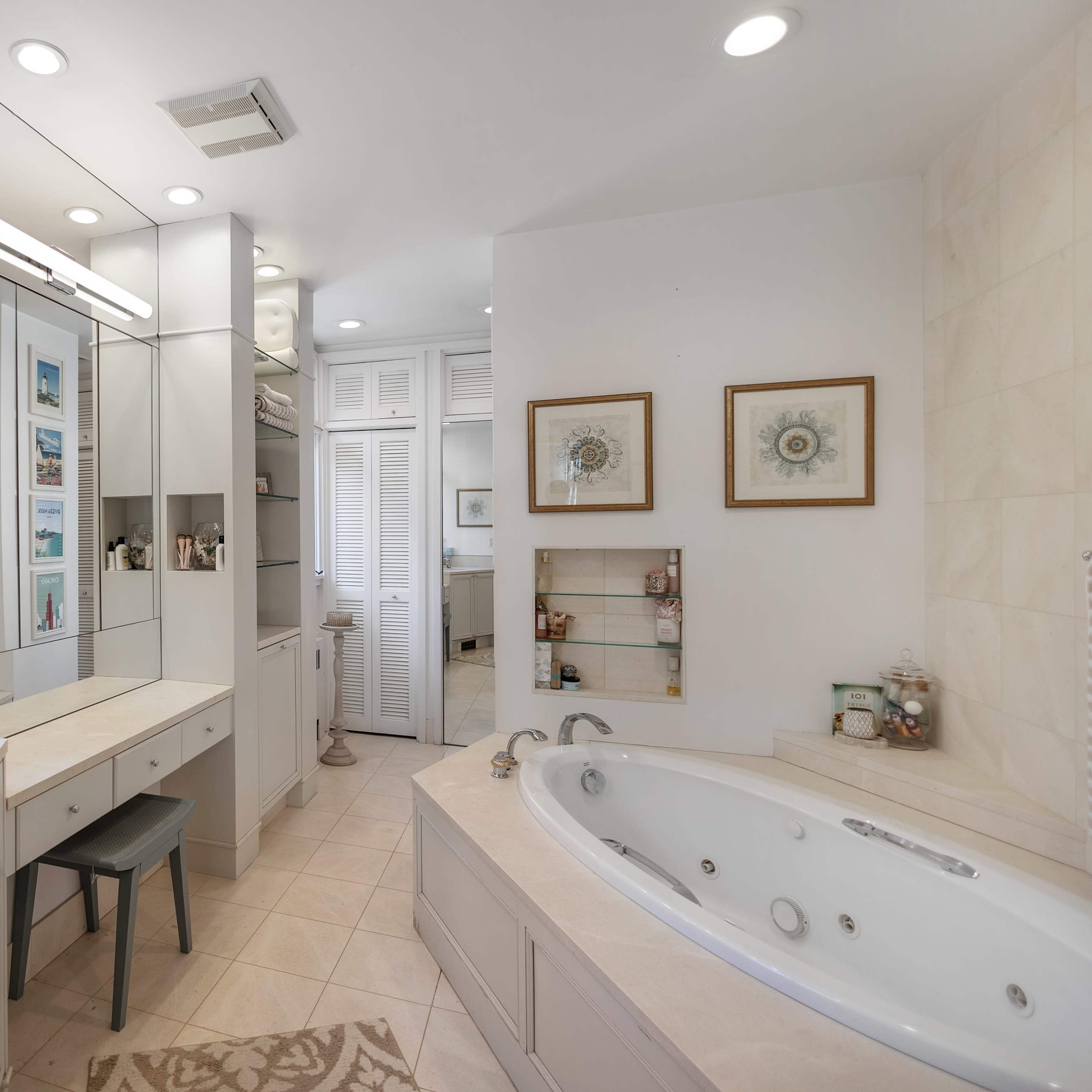 A modern bathroom featuring a large bathtub, a vanity area with a mirror, and storage shelves, all illuminated by soft lighting.