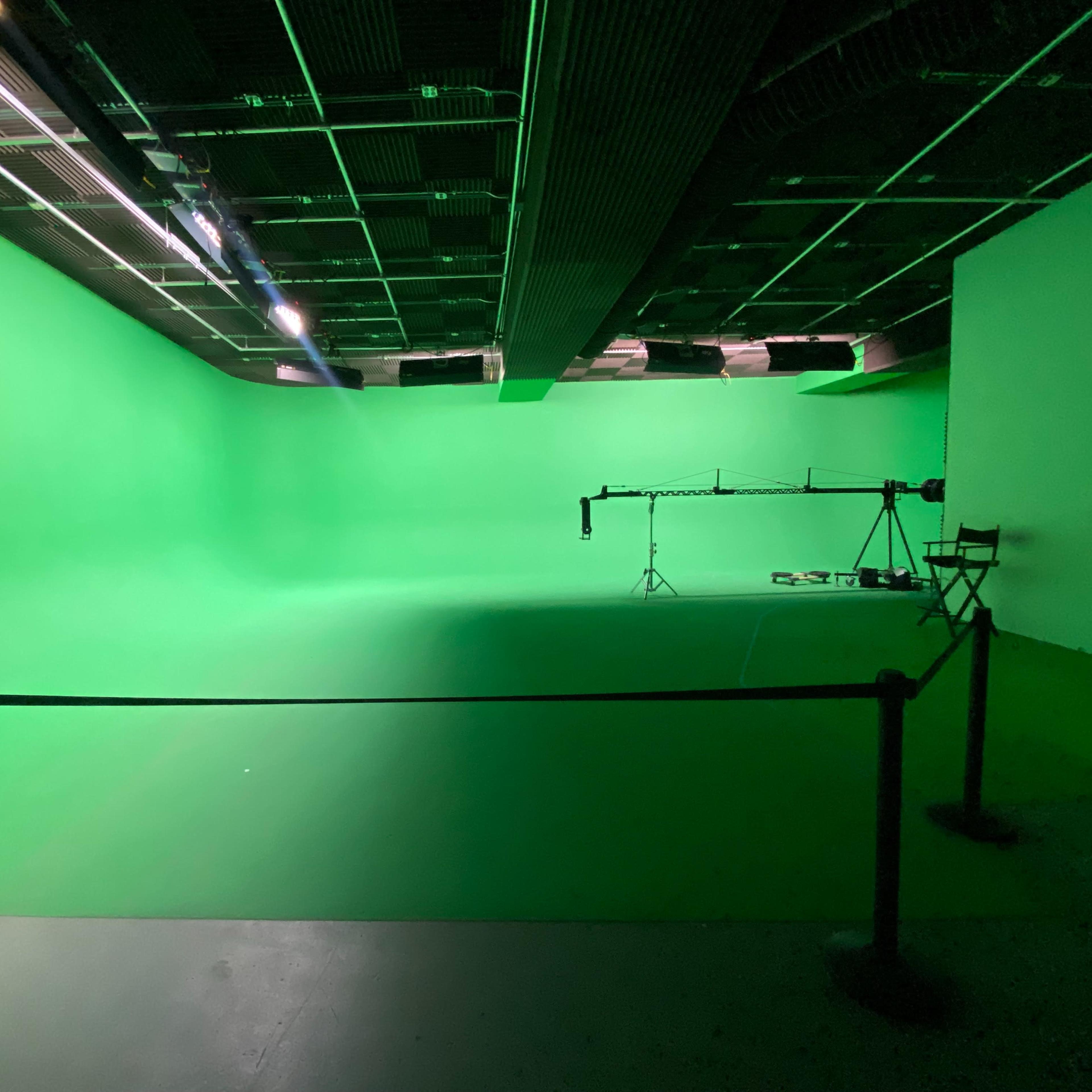 An empty green screen studio with adjustable lighting and a camera setup in the background.