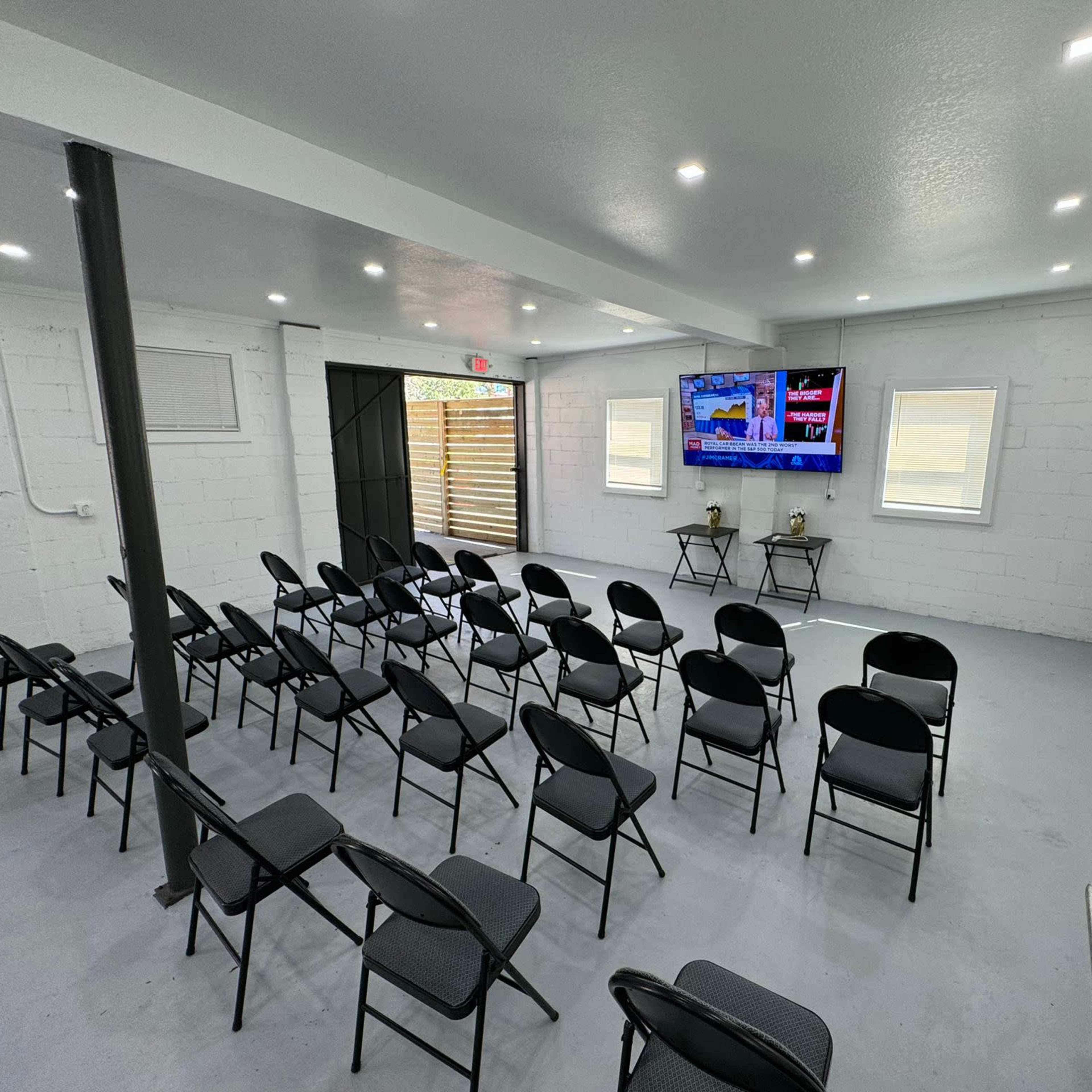 A neatly arranged meeting room with black folding chairs facing two large screens mounted on a white wall.
