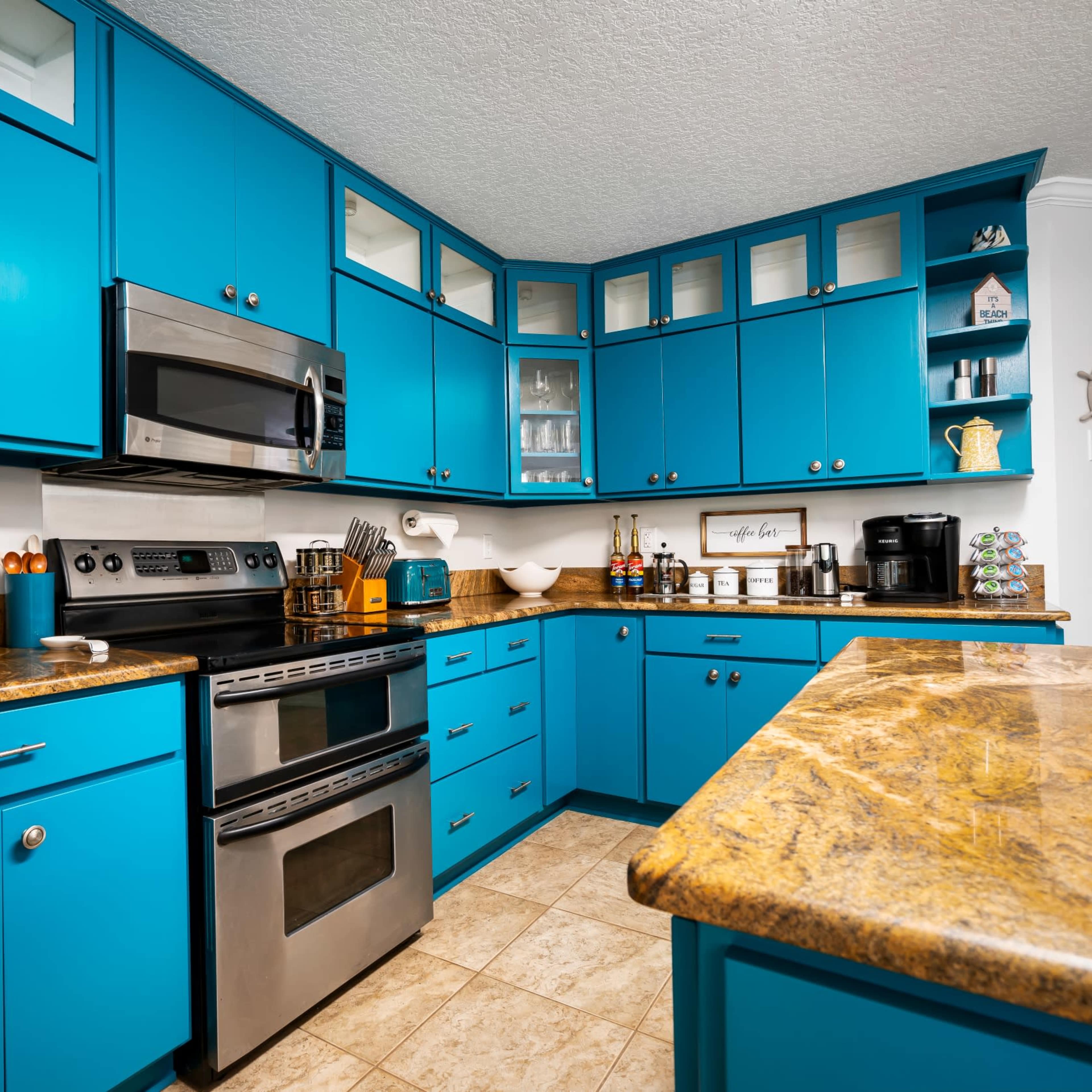 A modern kitchen with bright blue cabinets, stainless steel appliances, and a granite countertop.