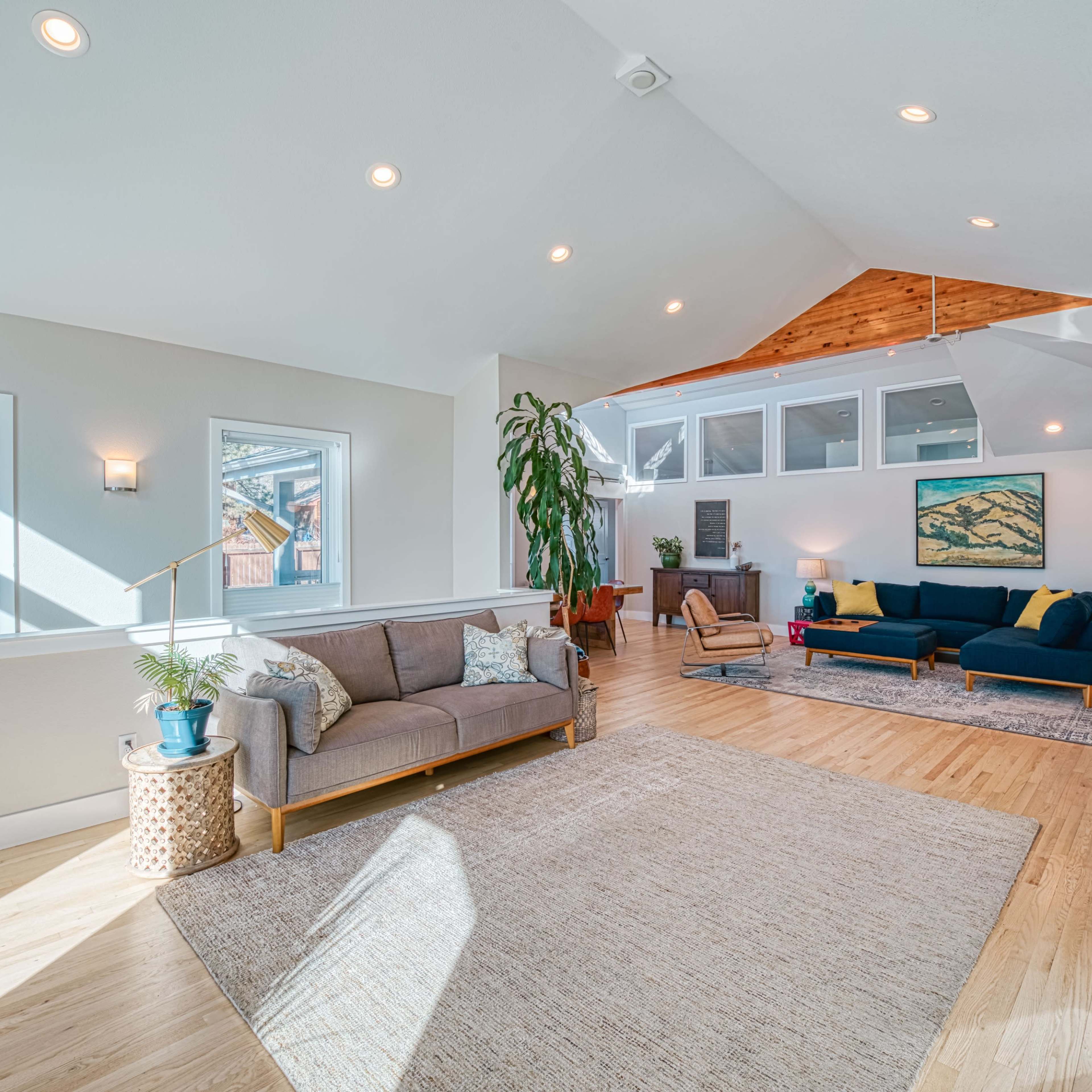 The bright, spacious interior features a living area with a sofa, armchair, and large windows, complemented by a light-colored rug and wooden accents.
