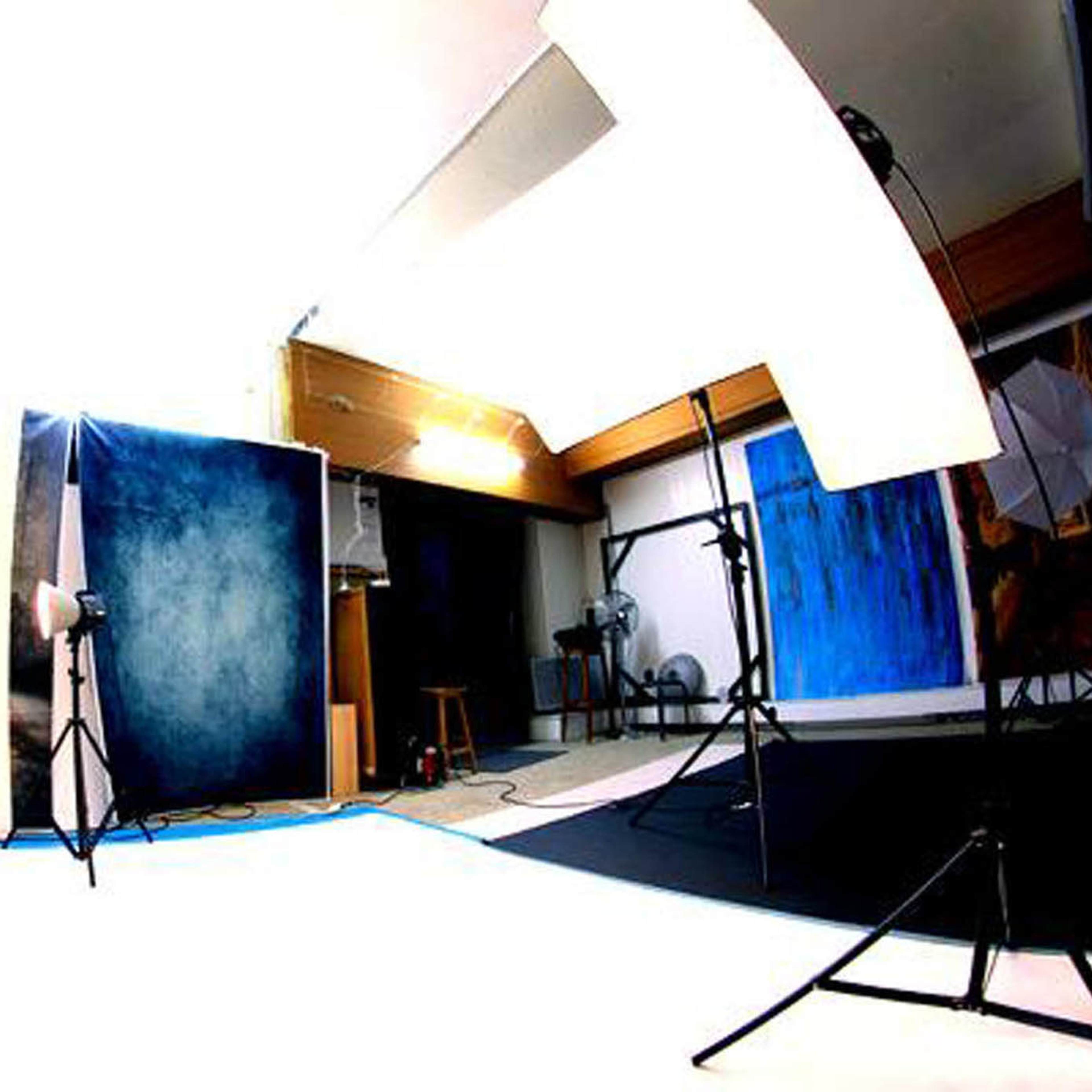 A photography studio with a blue backdrop, lighting equipment, and a stool in the corner.