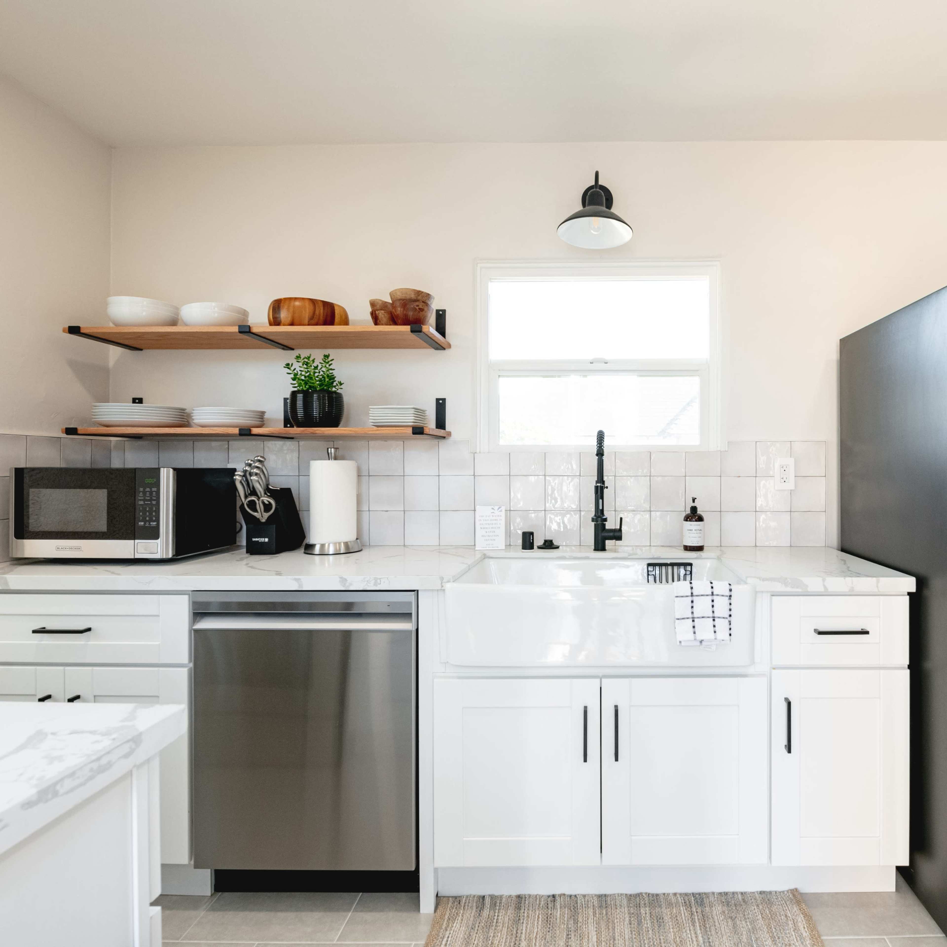 A modern kitchen featuring white cabinets, stainless steel appliances, and a farmhouse sink with open shelving above.