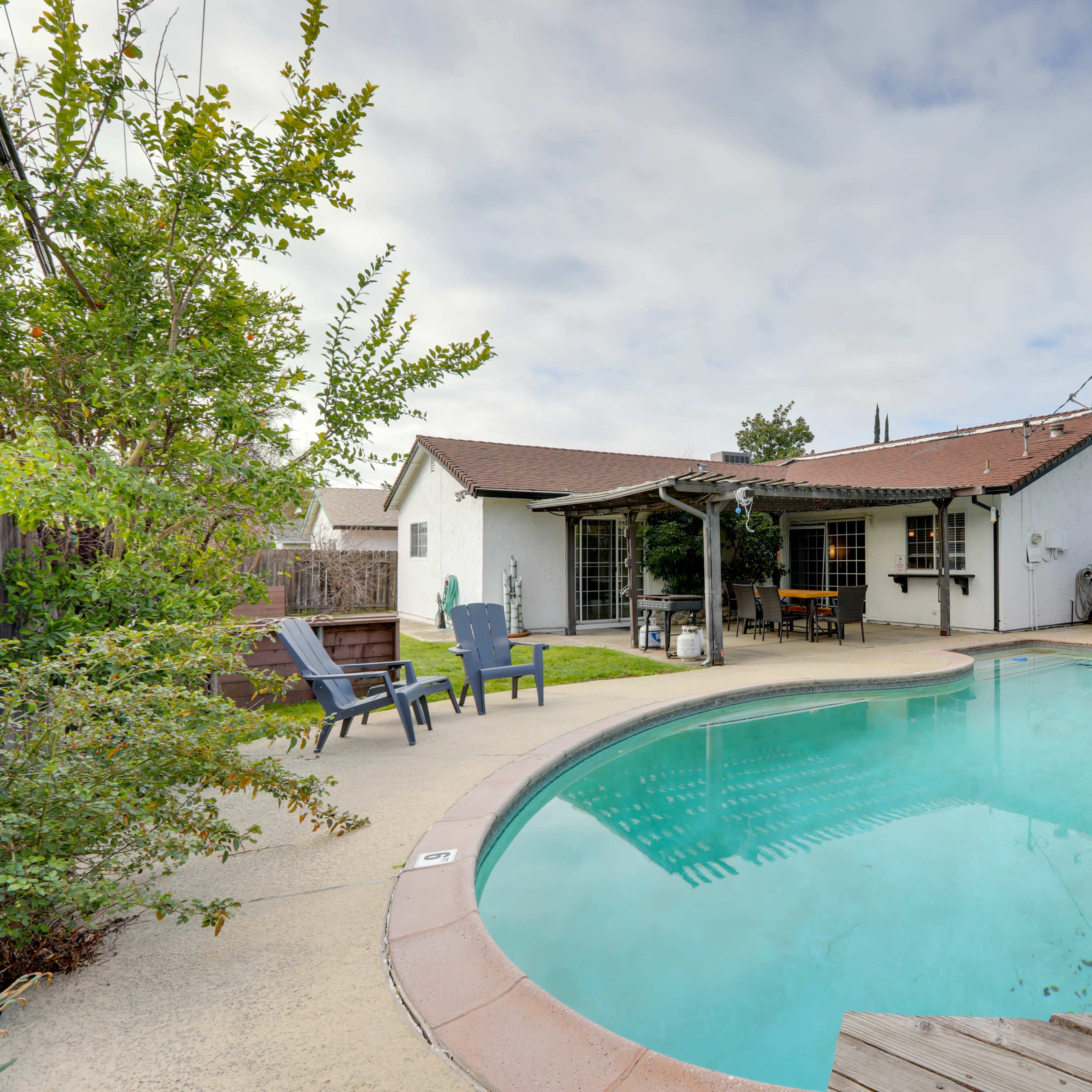 A backyard with a swimming pool, a wooden deck, and a single-story house with a covered patio.