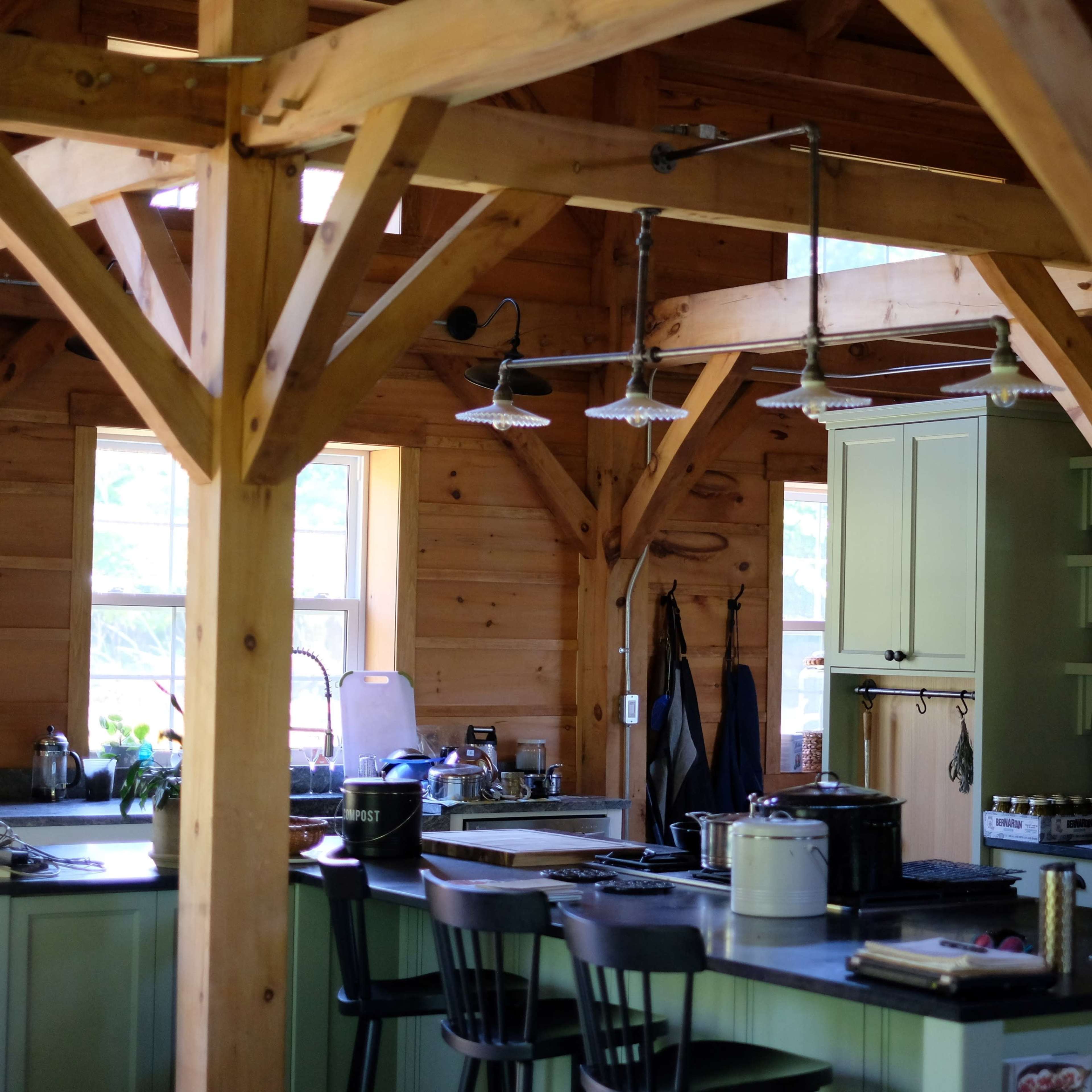 A spacious wooden kitchen with green cabinetry and a central island, featuring wooden beams and large windows that let in natural light.