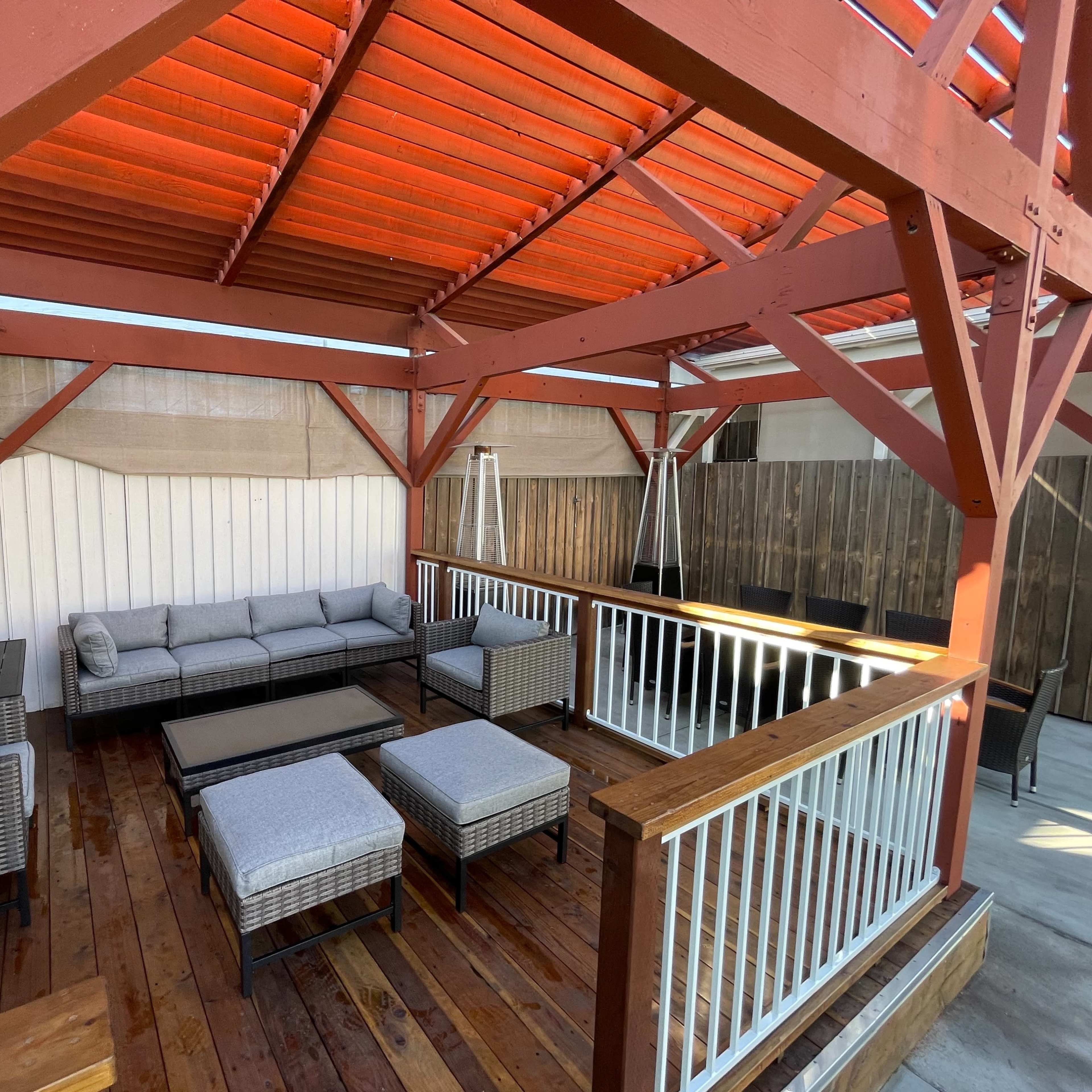 A covered outdoor seating area features a sofa set, coffee table, and additional seating on a wooden deck.