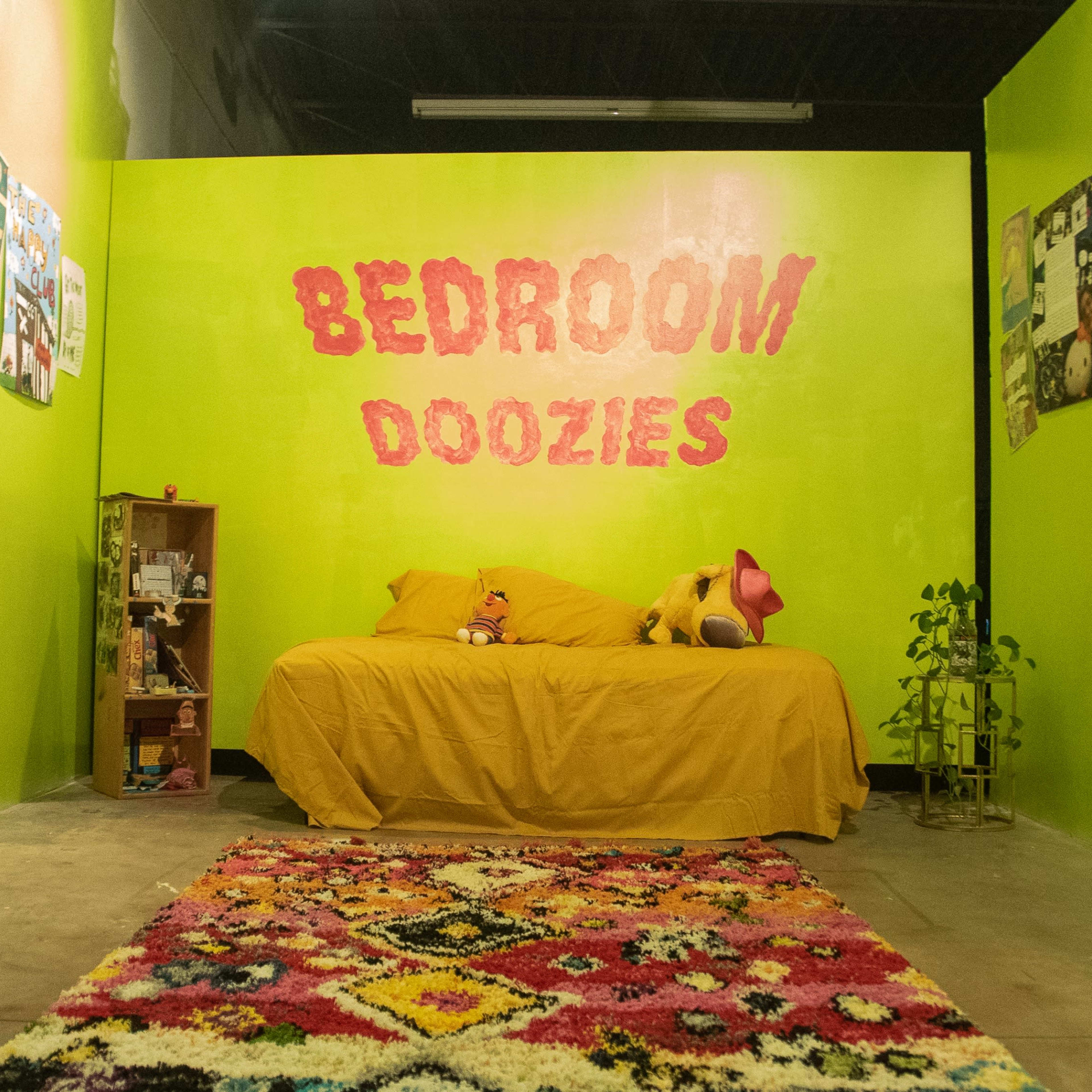 A small room with bright green walls, a yellow bedspread, a colorful patterned rug, and posters adorning the walls.