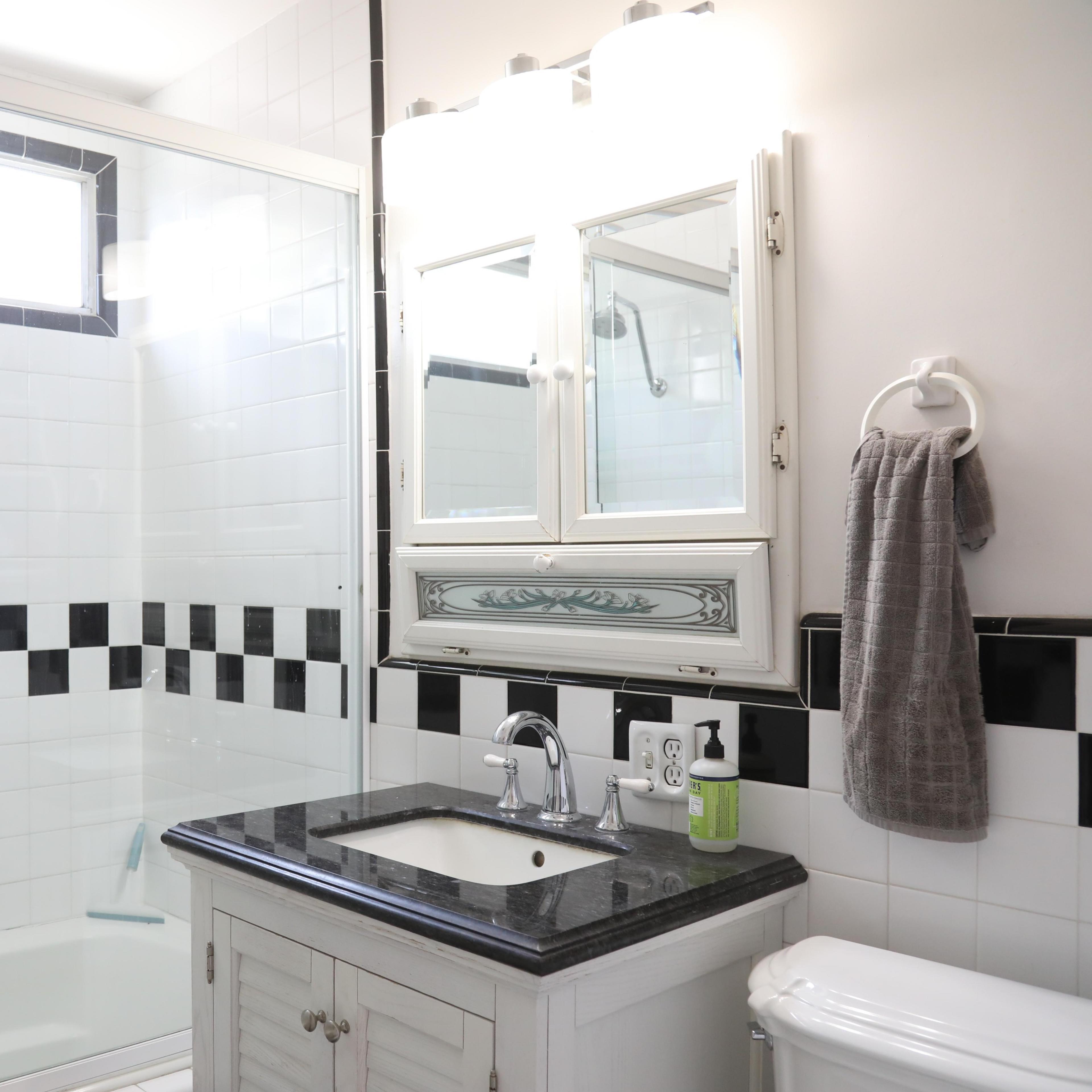 A modern bathroom featuring a glass shower enclosure, a sink with a dark countertop, and a wall mounted mirror above the sink.