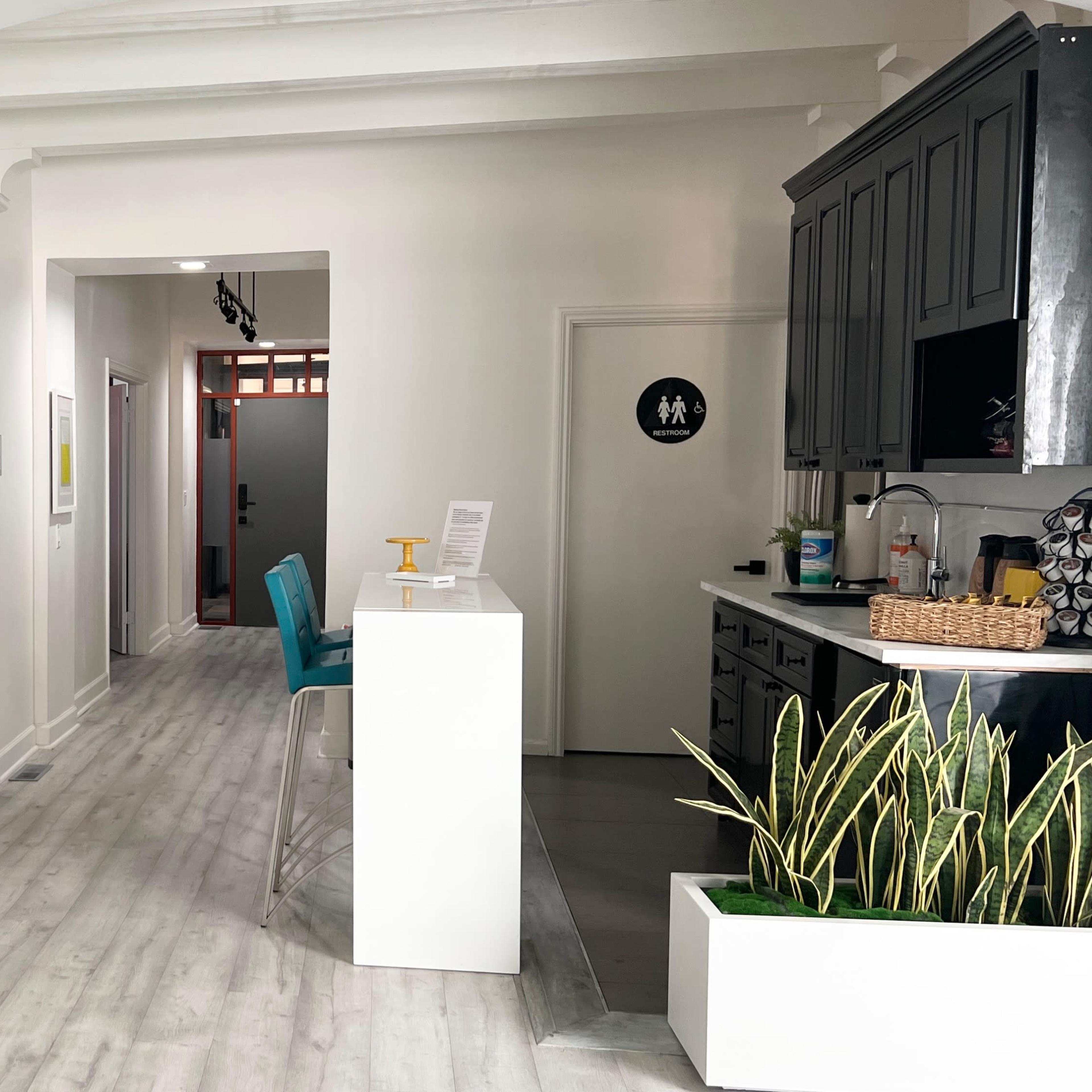 A modern, airy interior space with a white bench, a reception area with a service counter, and a corridor leading to additional rooms.
