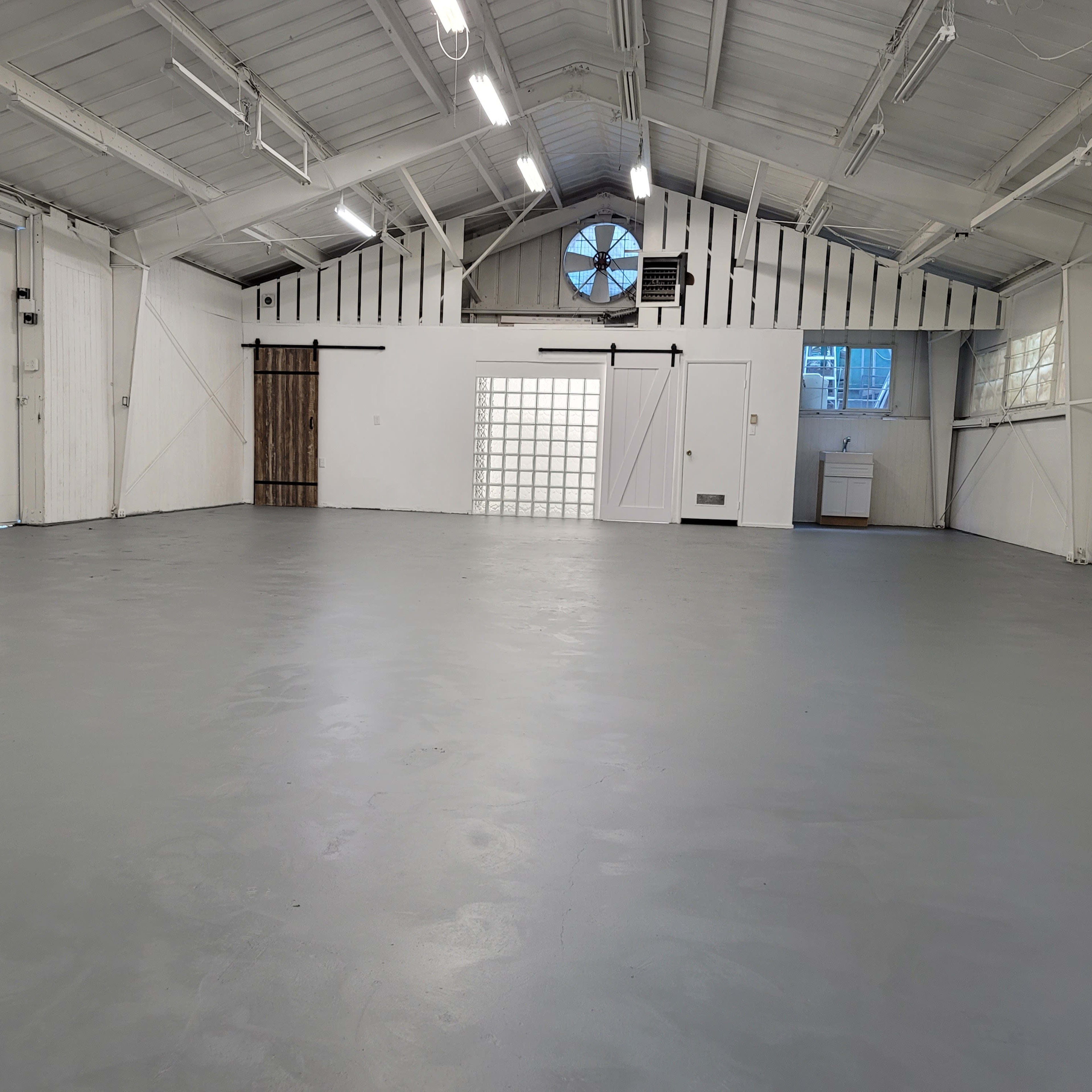 An empty industrial space with gray flooring and large windows allowing natural light to enter.