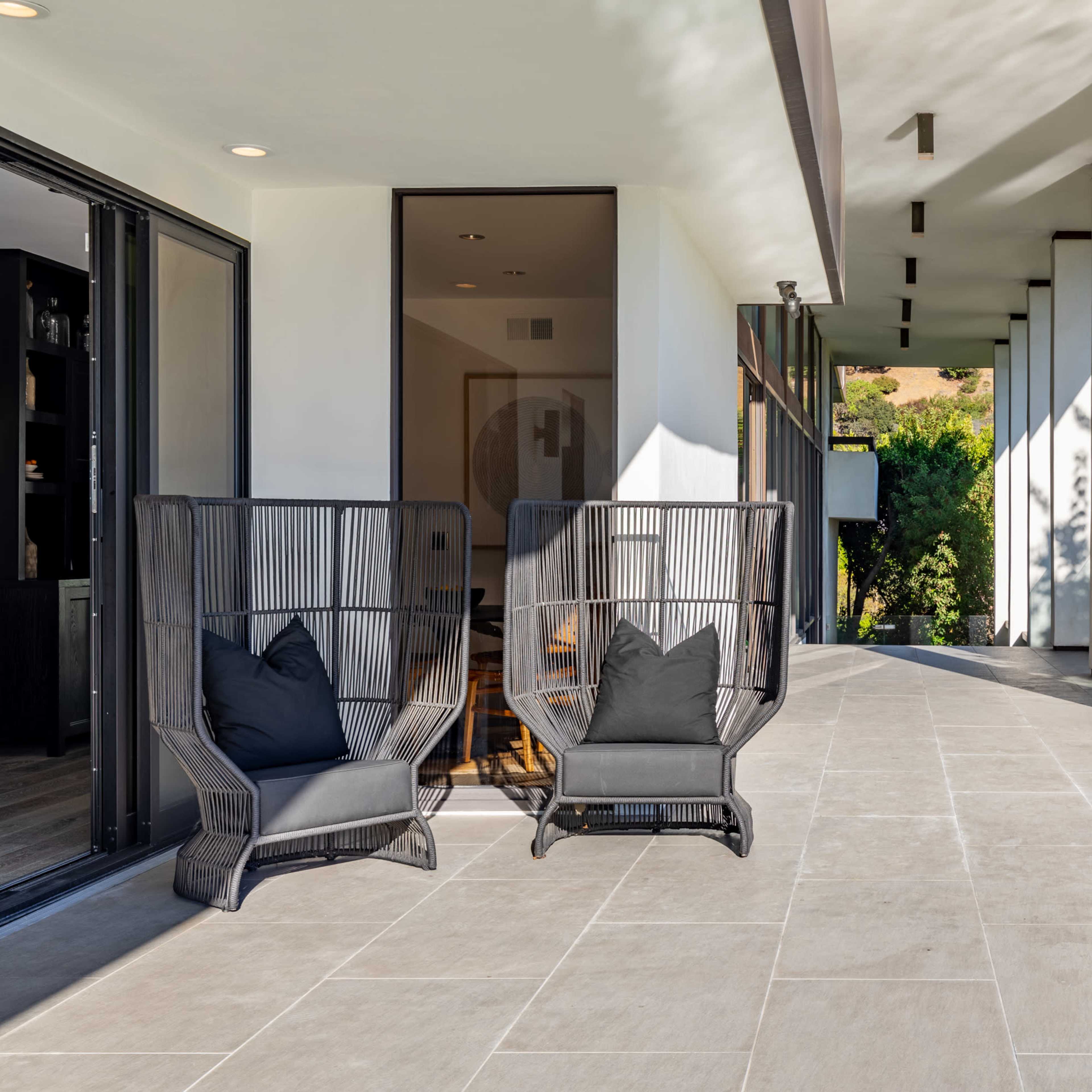 A modern patio with two black wicker chairs facing a swimming pool and greenery in the background.