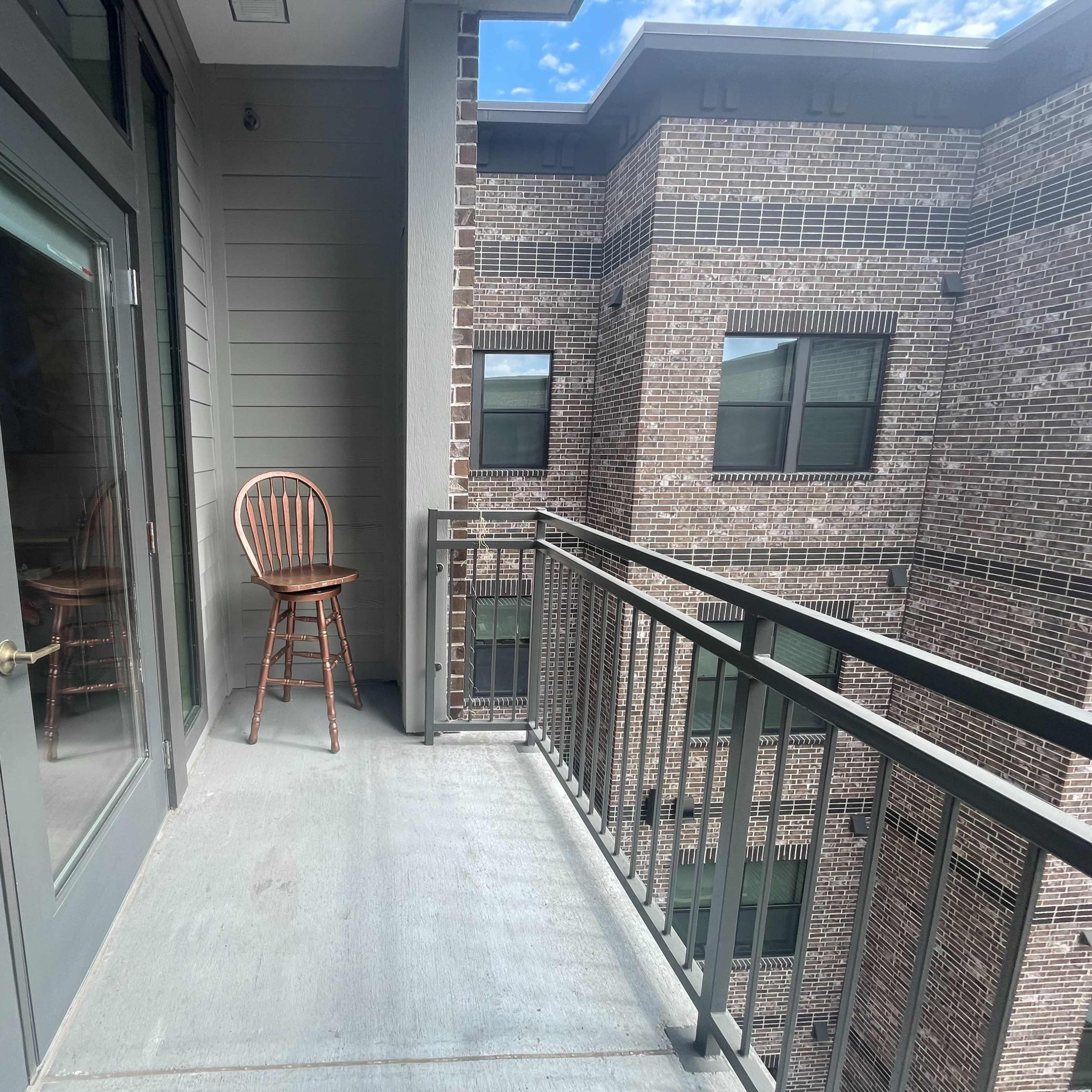 A small balcony with a wooden chair and a view of brick buildings nearby.