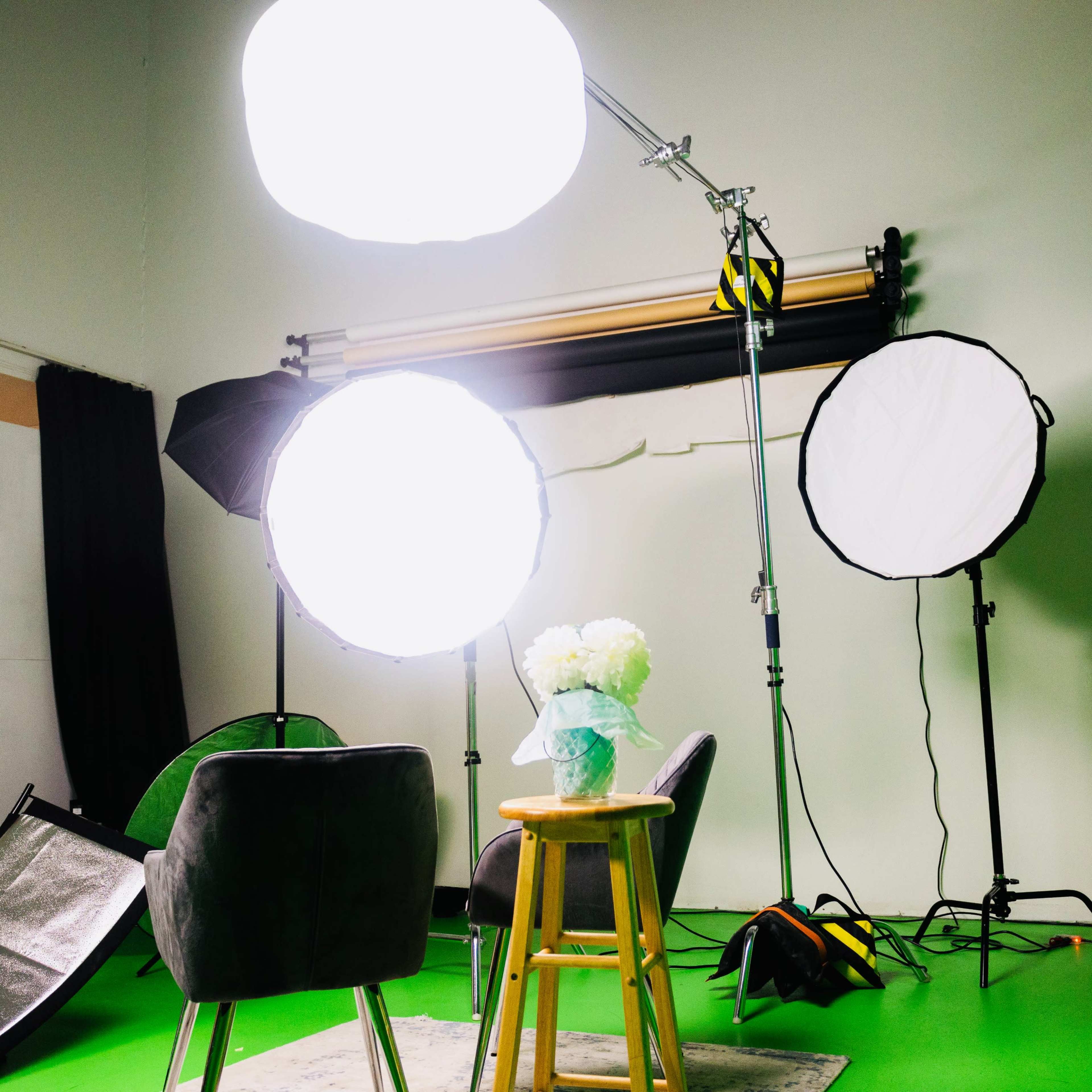 A photography studio setup features softbox lights, a small table with a vase of flowers, and a green backdrop.