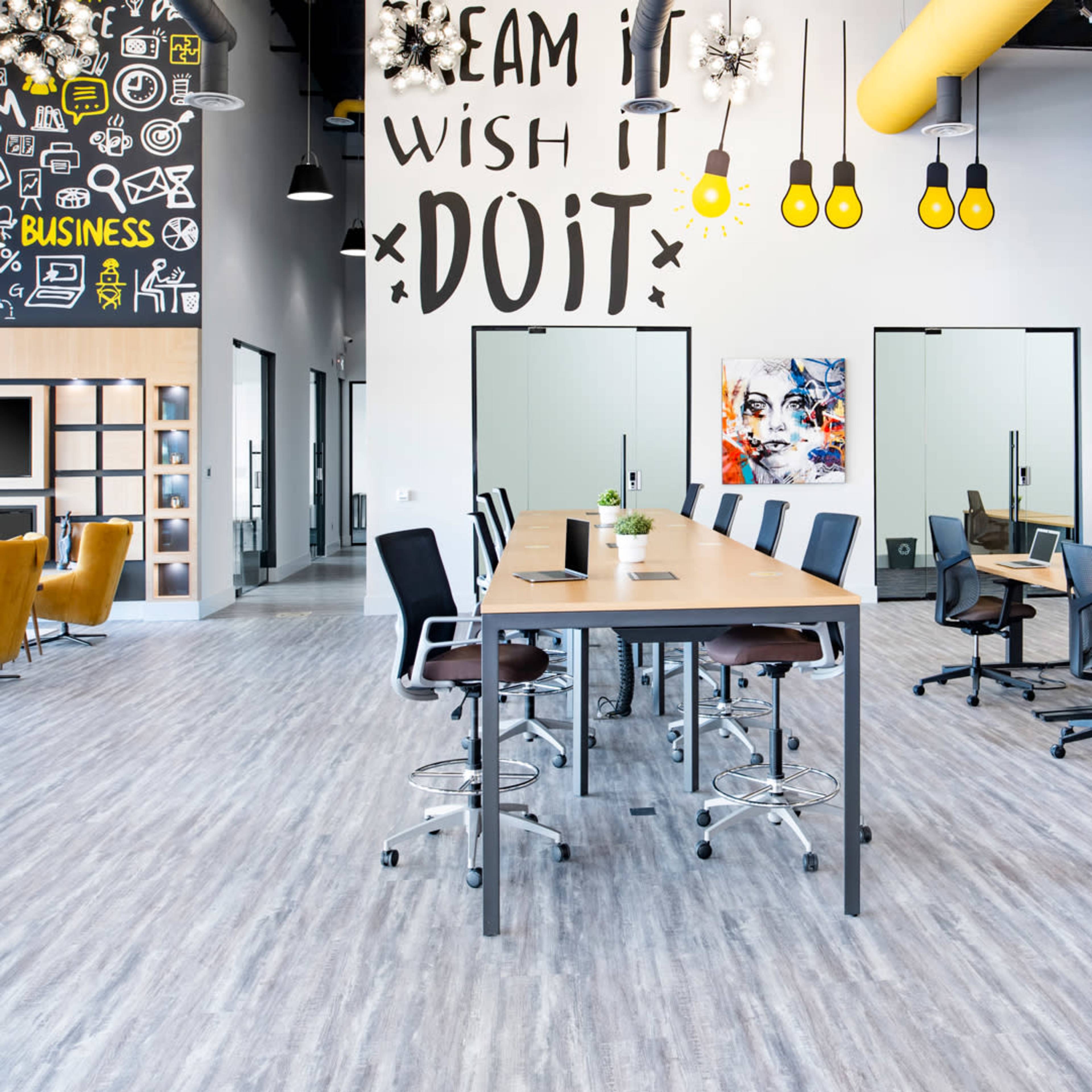 A modern office space with multiple desks, chairs, and glass meeting rooms, decorated with inspirational wall art.