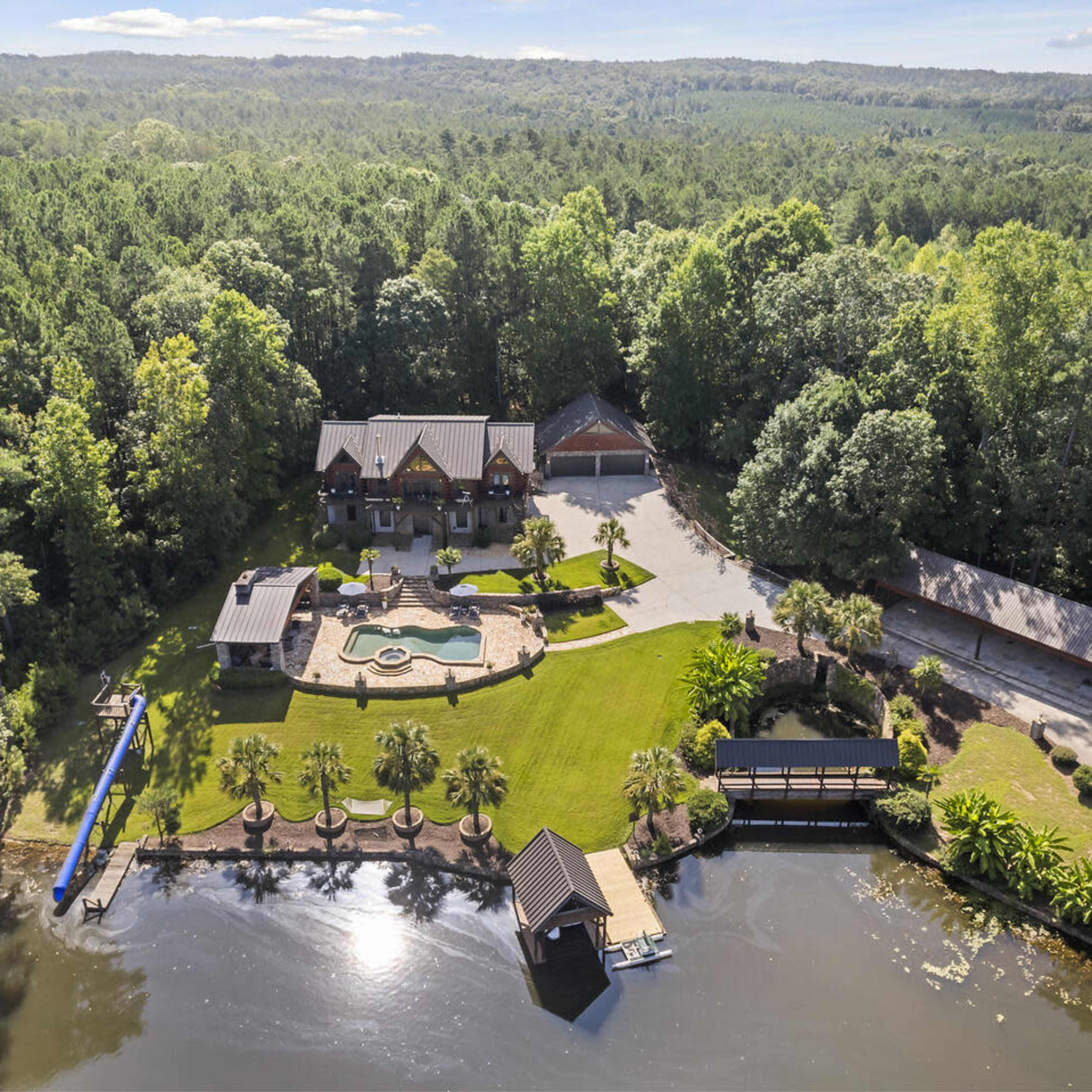 A large house with a swimming pool and landscaped grounds situated near a body of water and surrounded by trees.