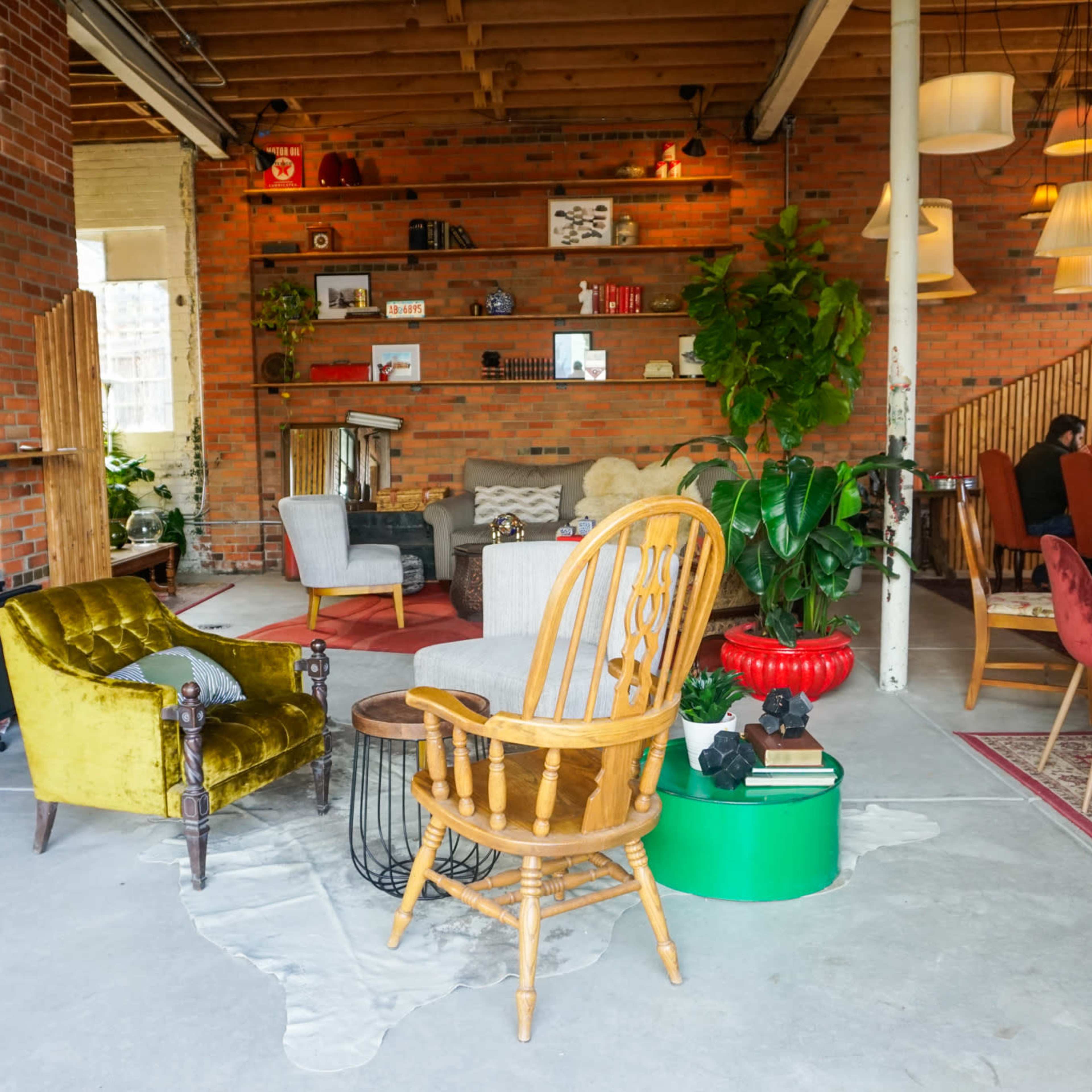 A cozy interior of a café featuring a mix of colorful seating, brick walls, and shelves adorned with decorative items.