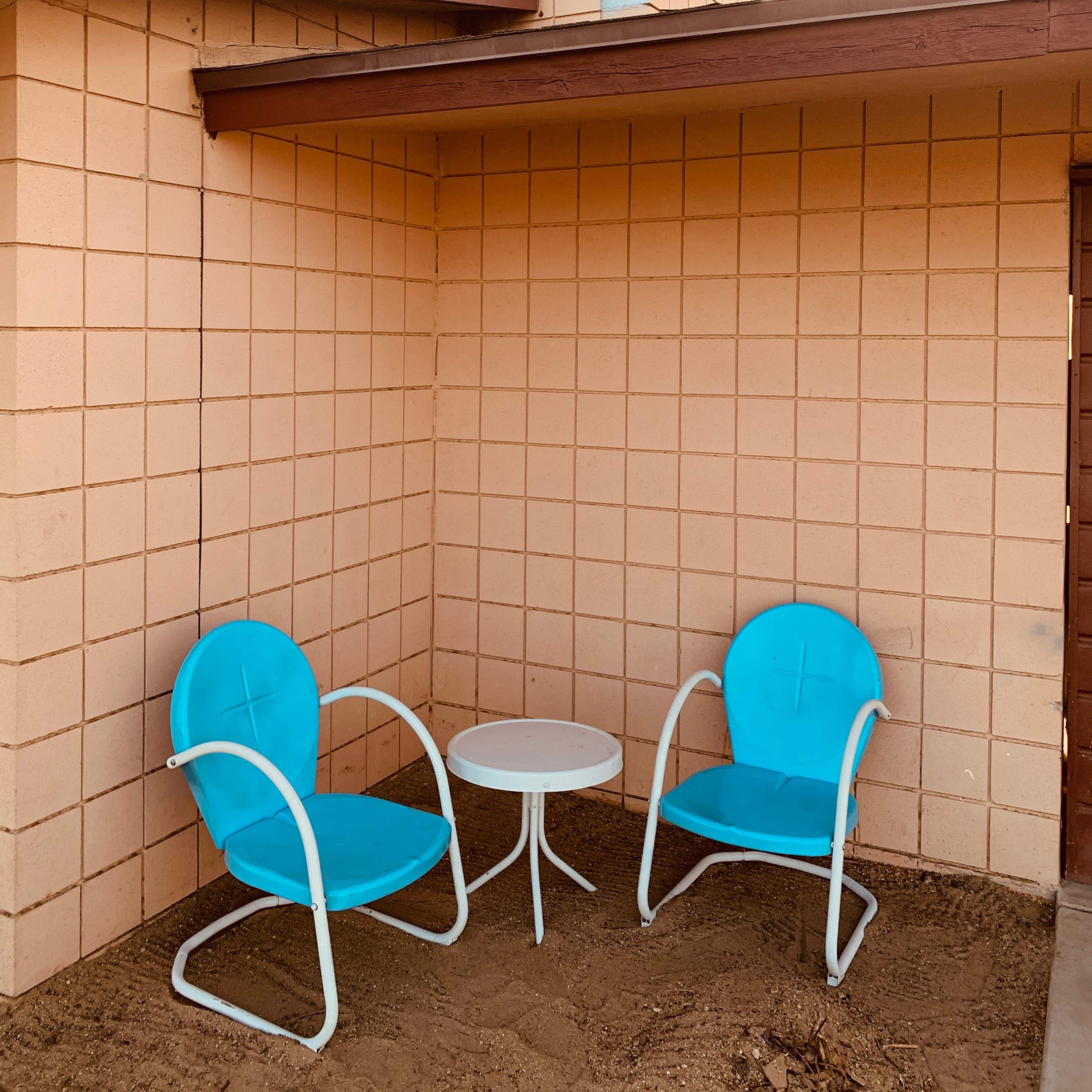 Two turquoise chairs and a small white table in a corner of a beige-block wall structure.