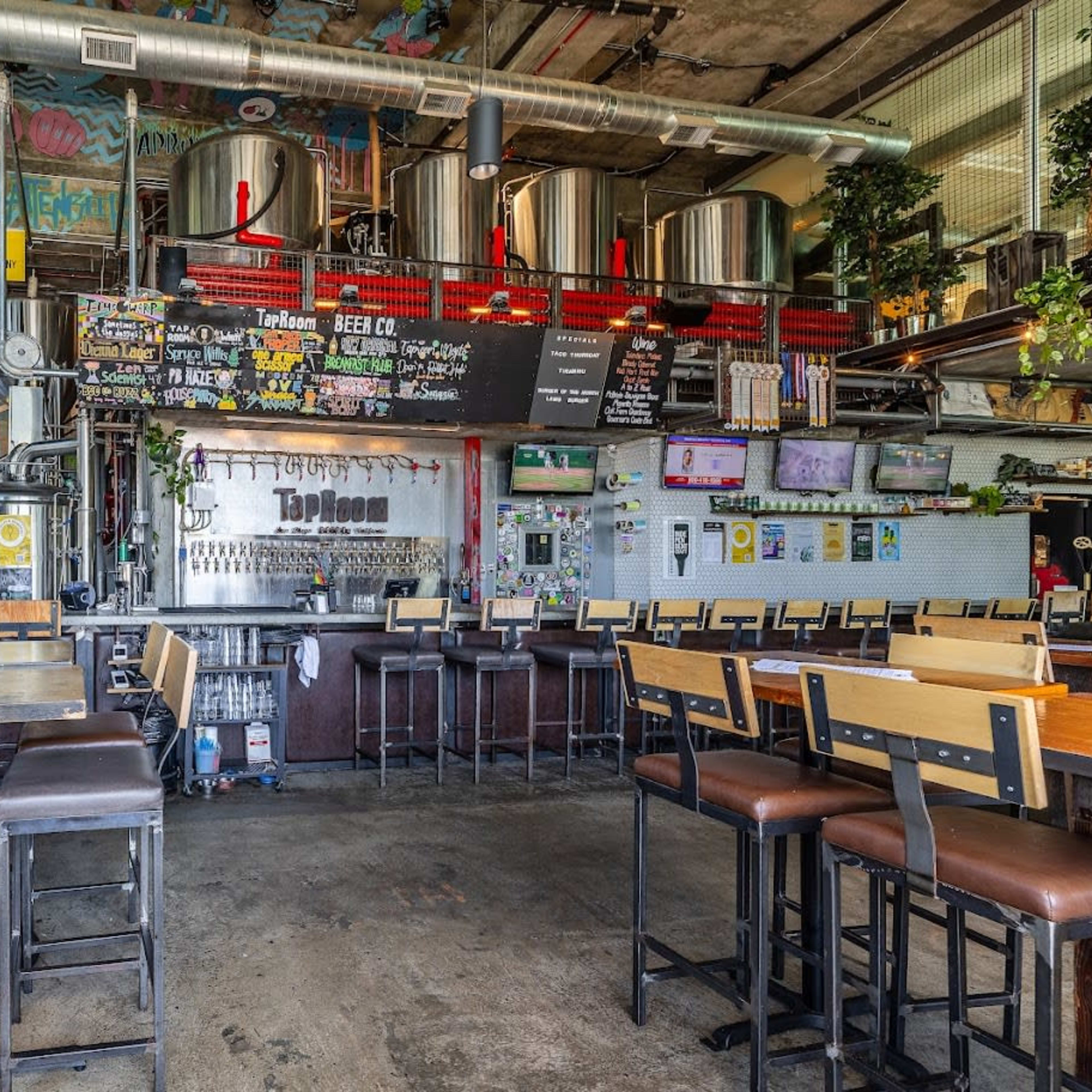 A spacious, industrial-style brewpub with metal brewing tanks, a long bar, and seating arranged at wooden tables.