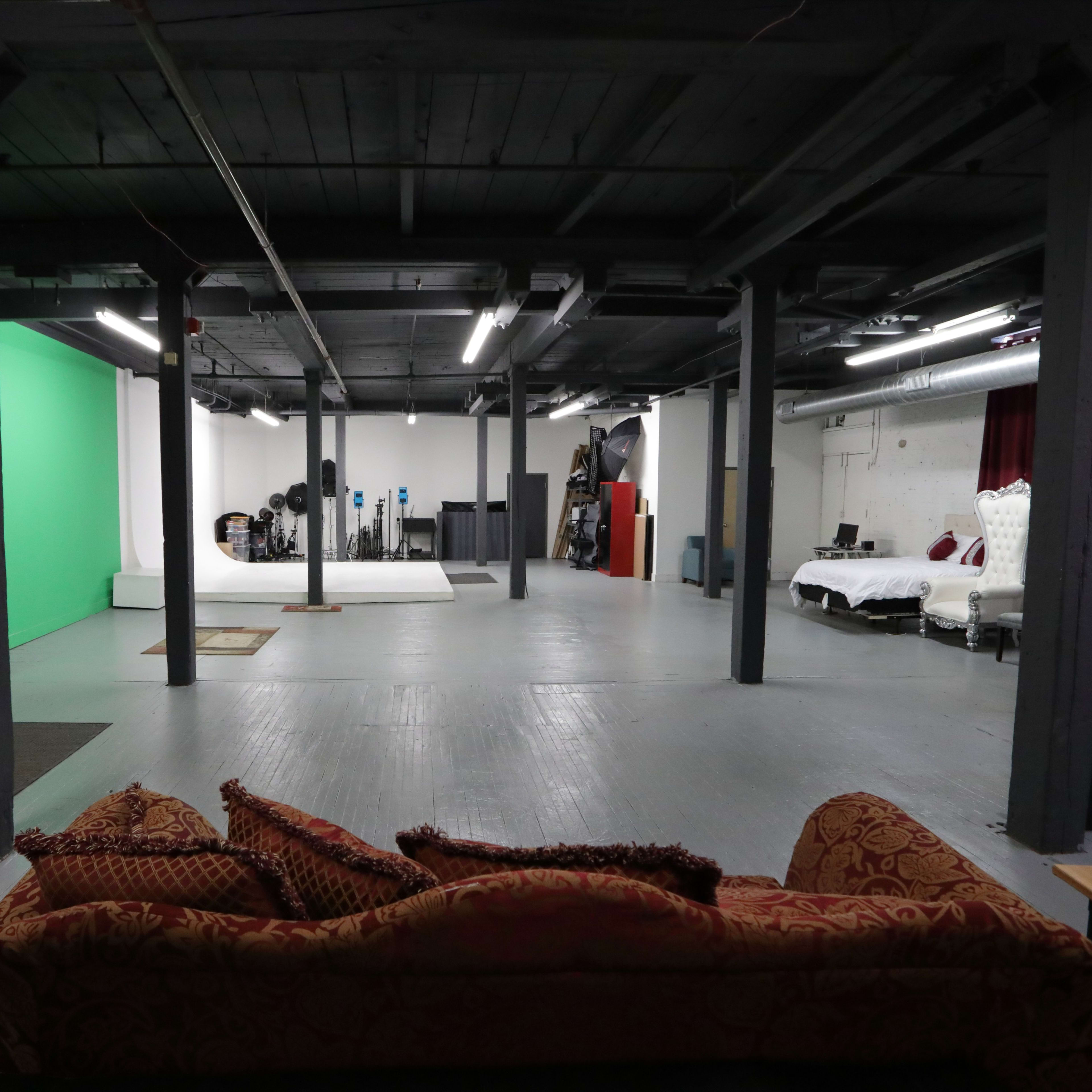 A large, open studio space with a green screen backdrop and various equipment along the walls, including a bed setup.