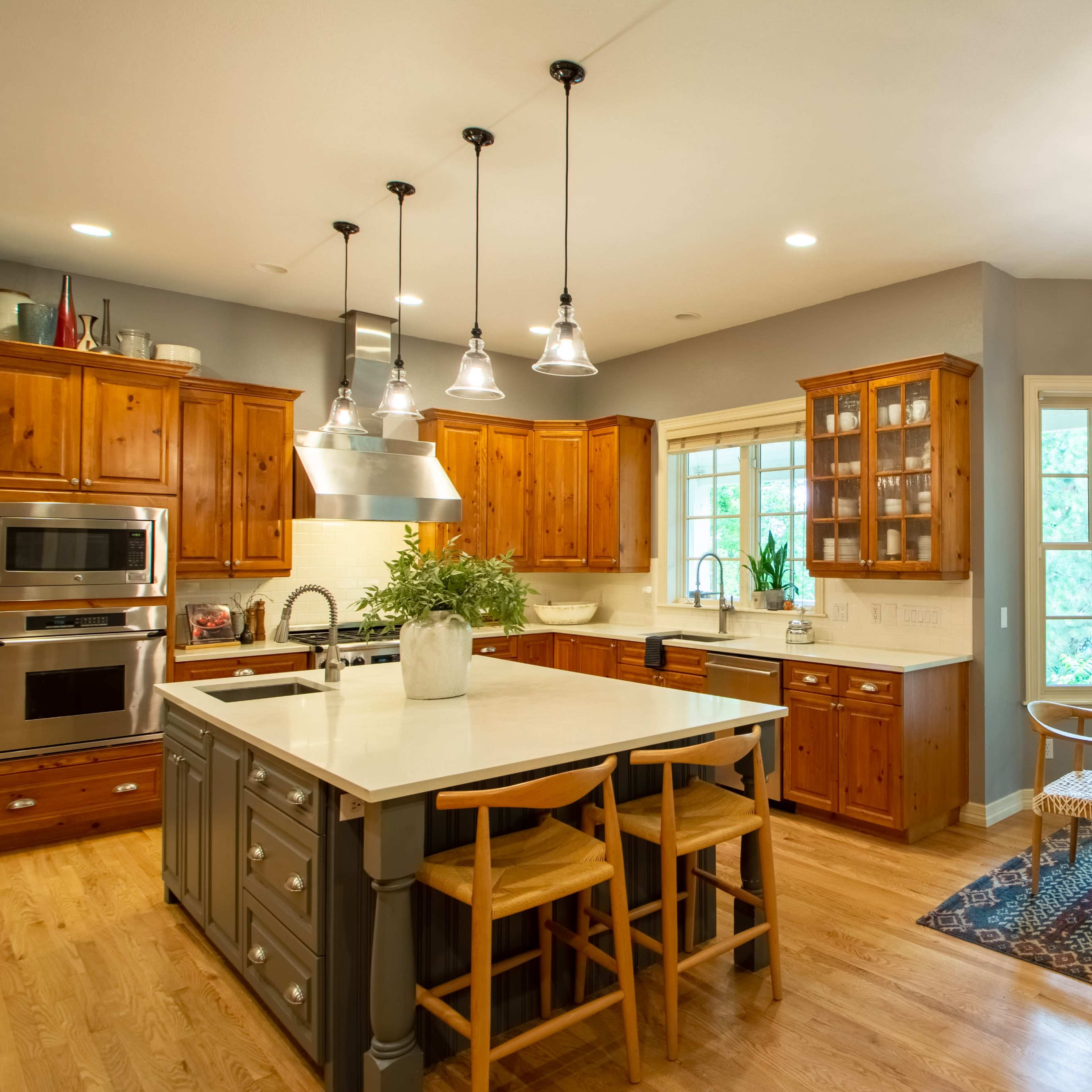 A modern kitchen with wooden cabinetry, an island with seating, and a dining area featuring a large table and a view of greenery through large windows.