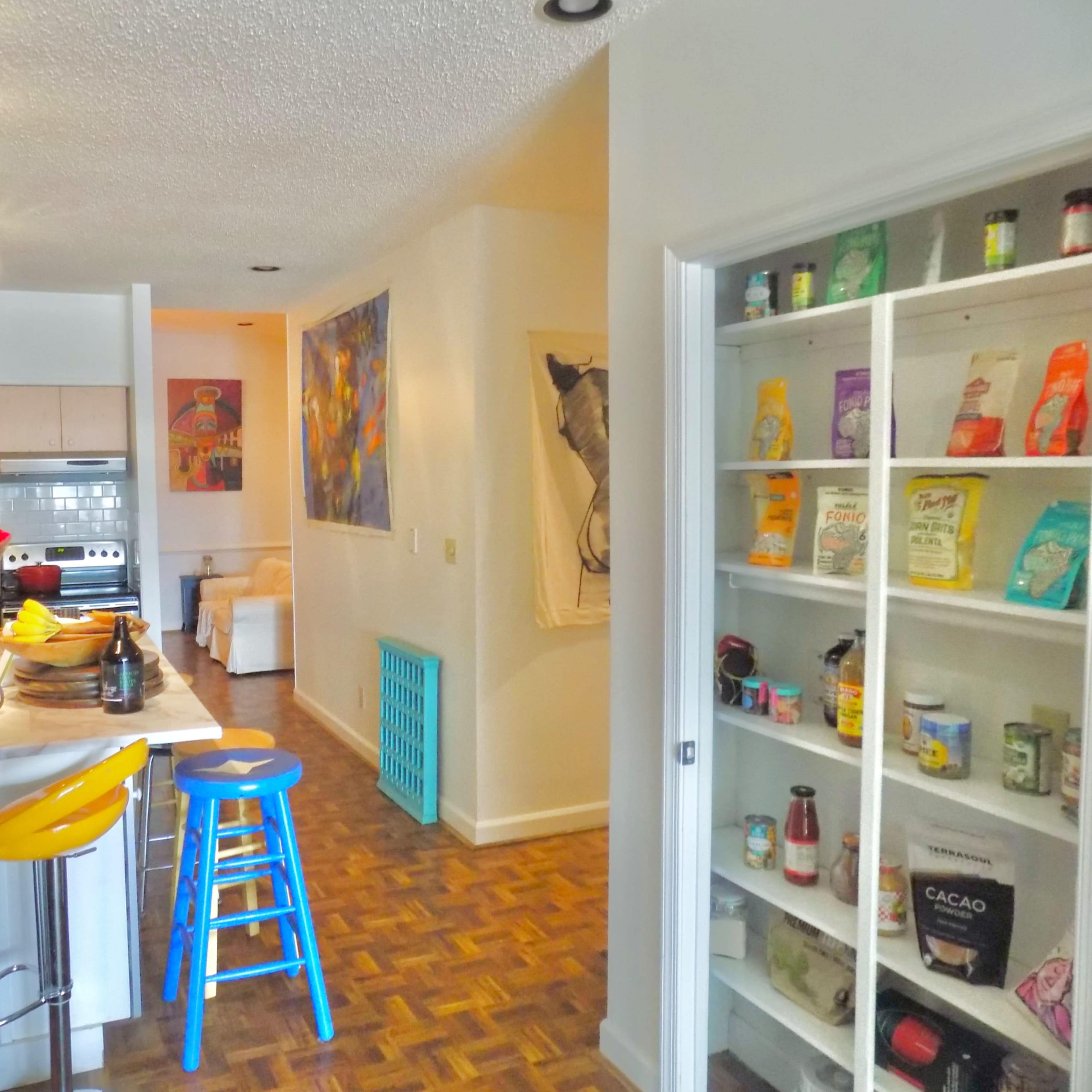 A modern kitchen with a dining area features a pantry filled with various food items and a small table with seating.