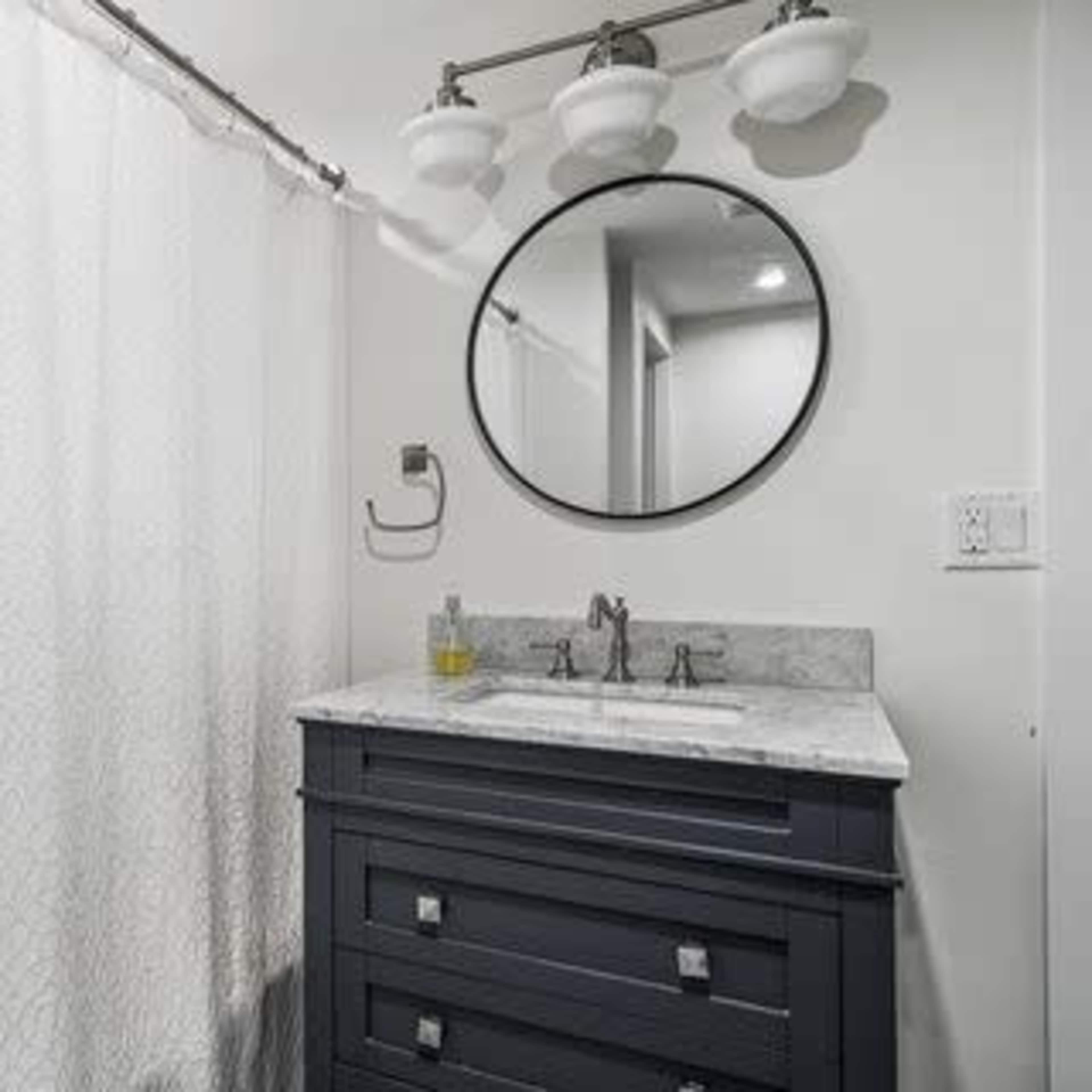 A modern bathroom featuring a dark gray vanity with a marble countertop, a circular mirror, and a shower area with a patterned curtain.