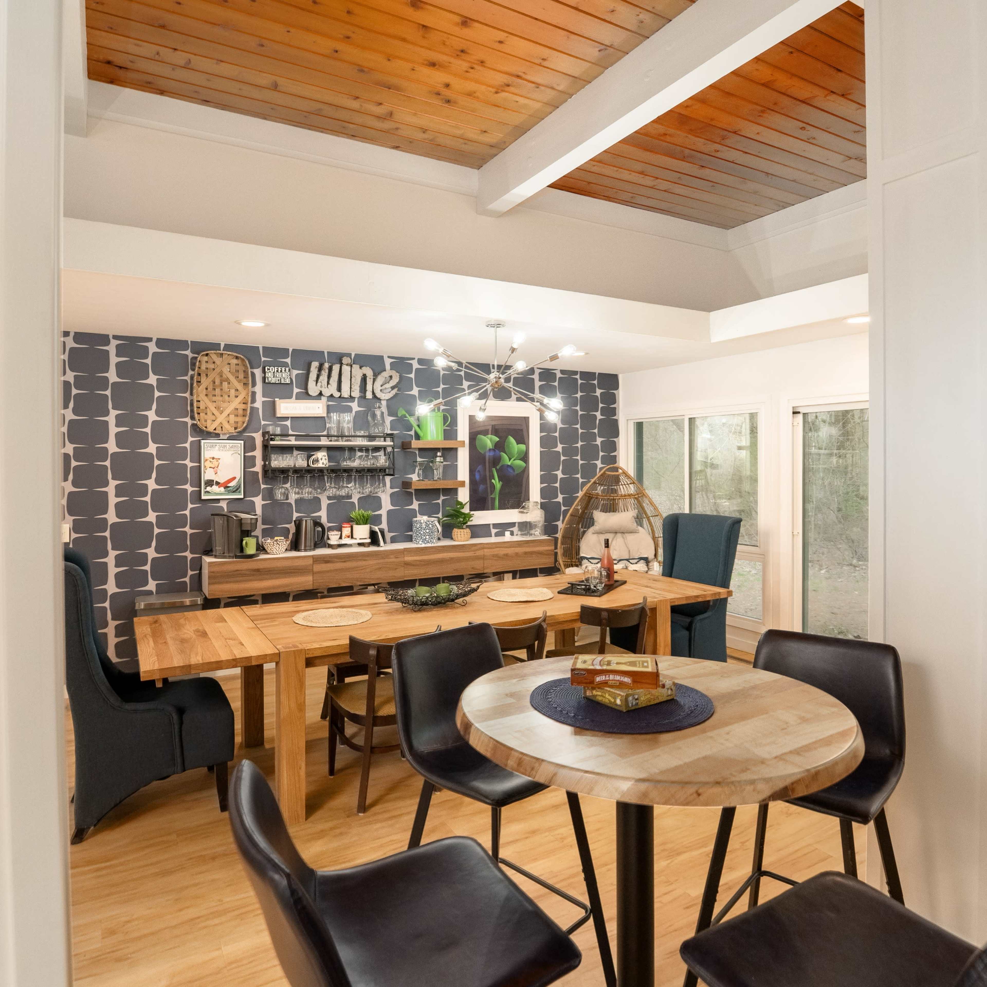 A modern dining area with a wooden table surrounded by chairs, a patterned accent wall, and large windows providing natural light.