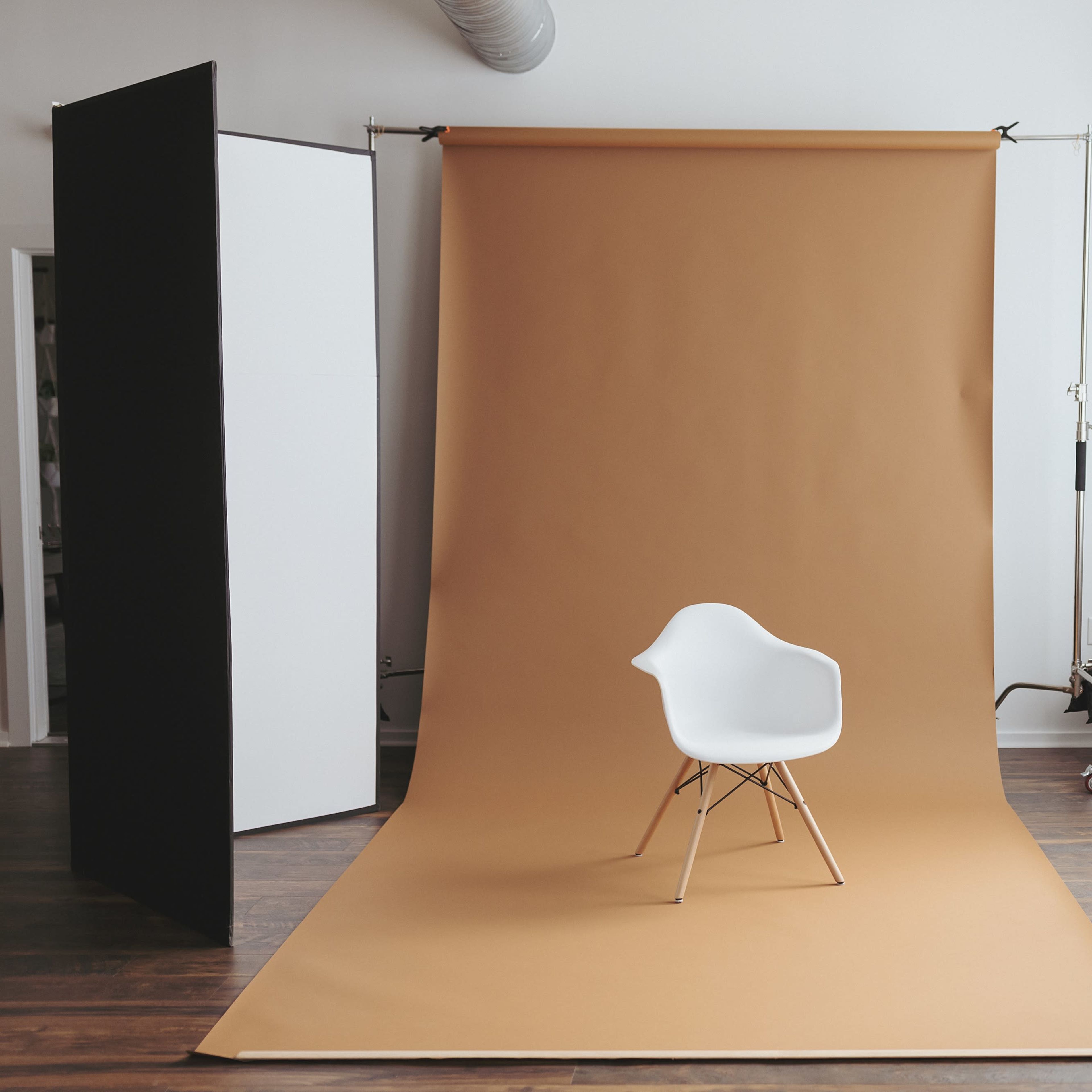 A white chair sits on a brown backdrop in a well-lit room with brick walls and large windows.
