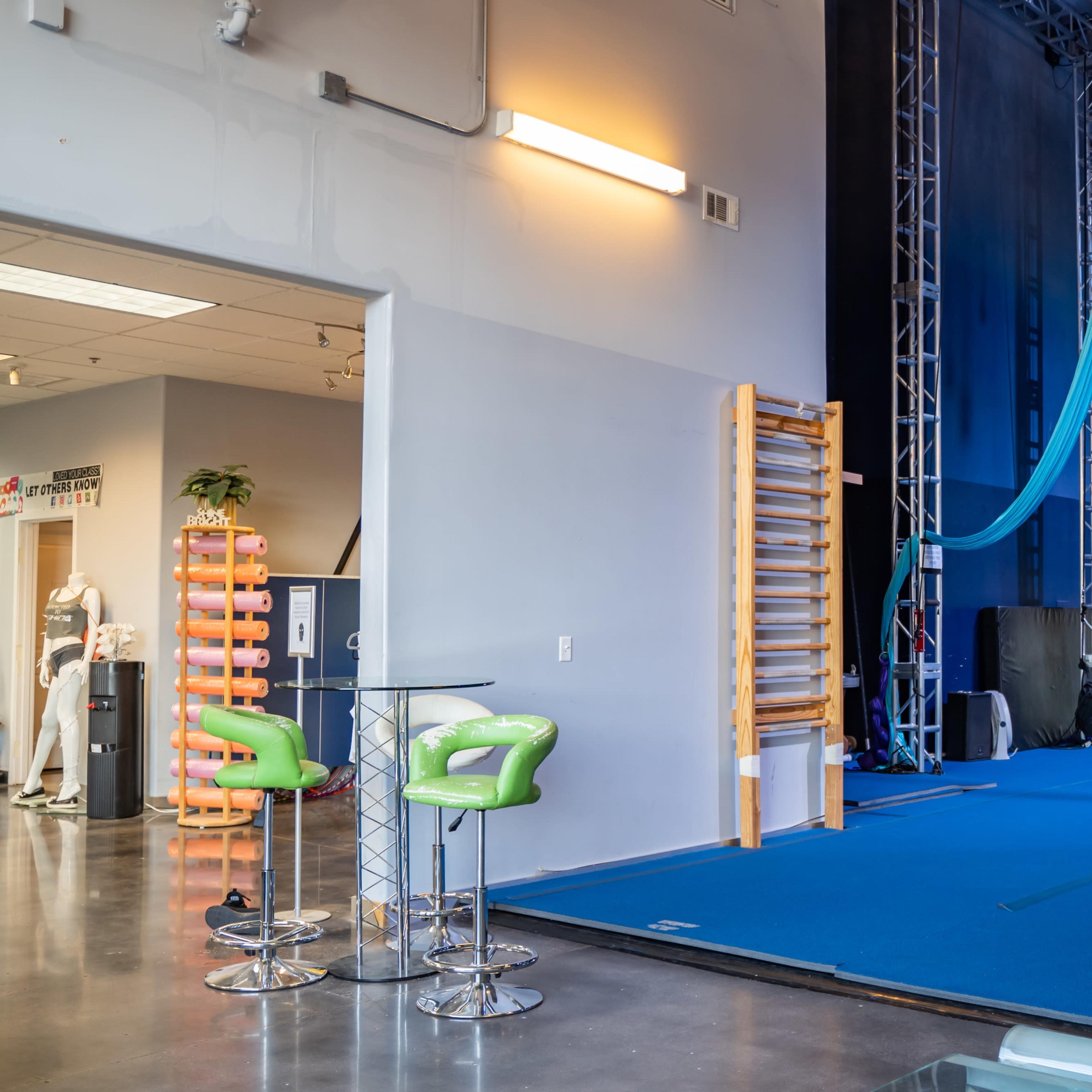 A gym space with blue mats, exercise equipment, and aerial silks hanging from the ceiling.