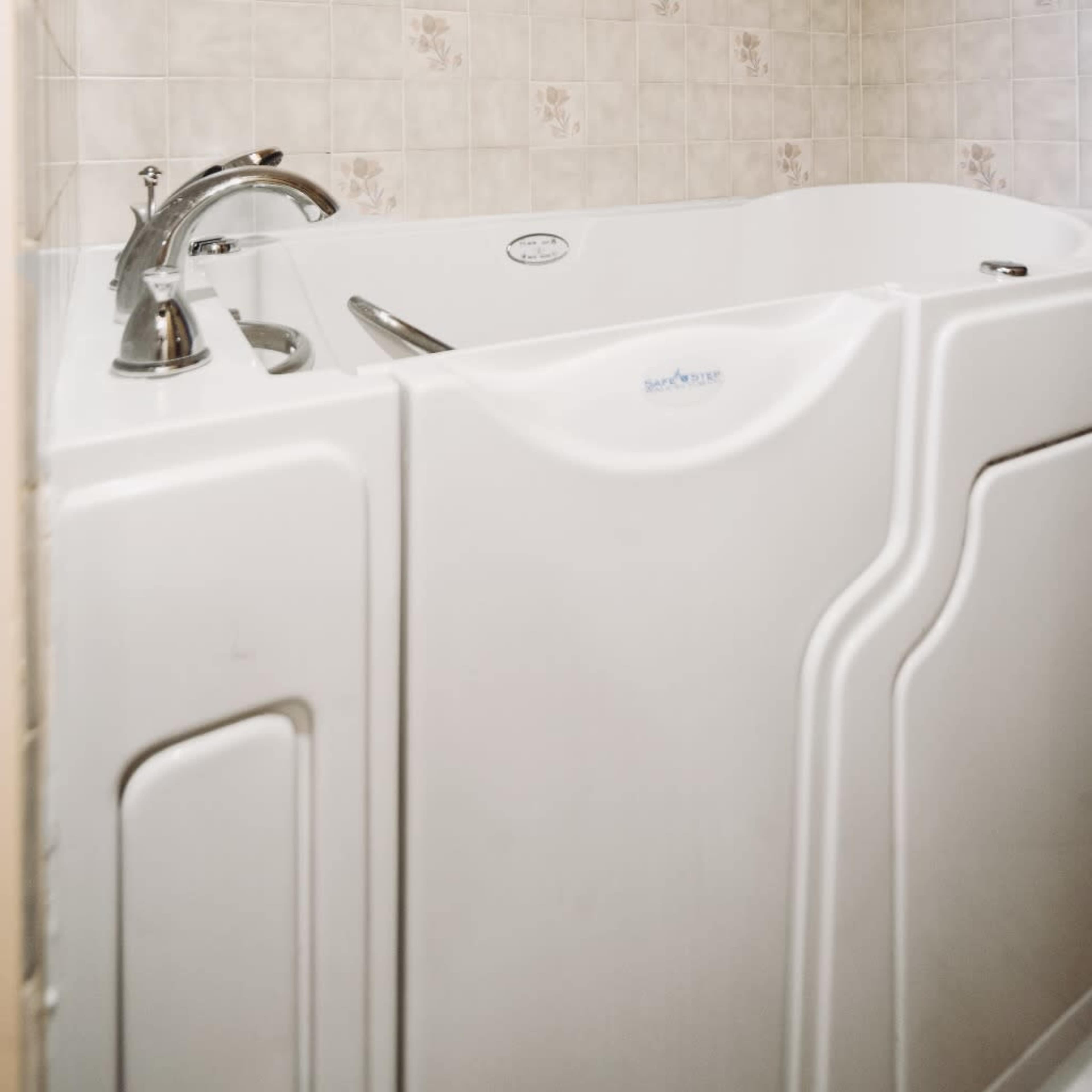 A walk-in bathtub with a sliding door, set against a tiled wall with floral patterns.
