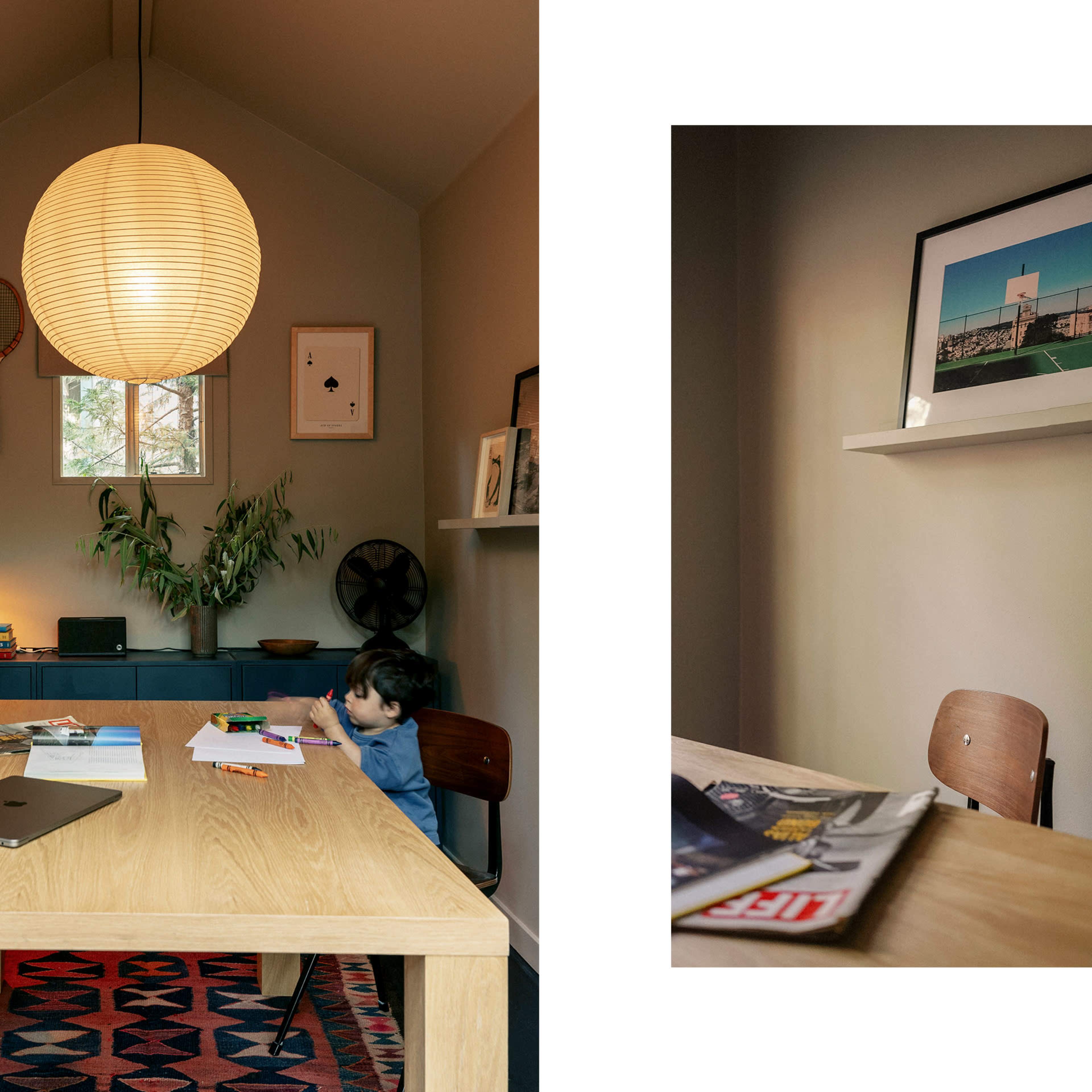 A child sits at a wooden table in a cozy room decorated with artwork and a large pendant light, while a shelf displays framed images and magazines.