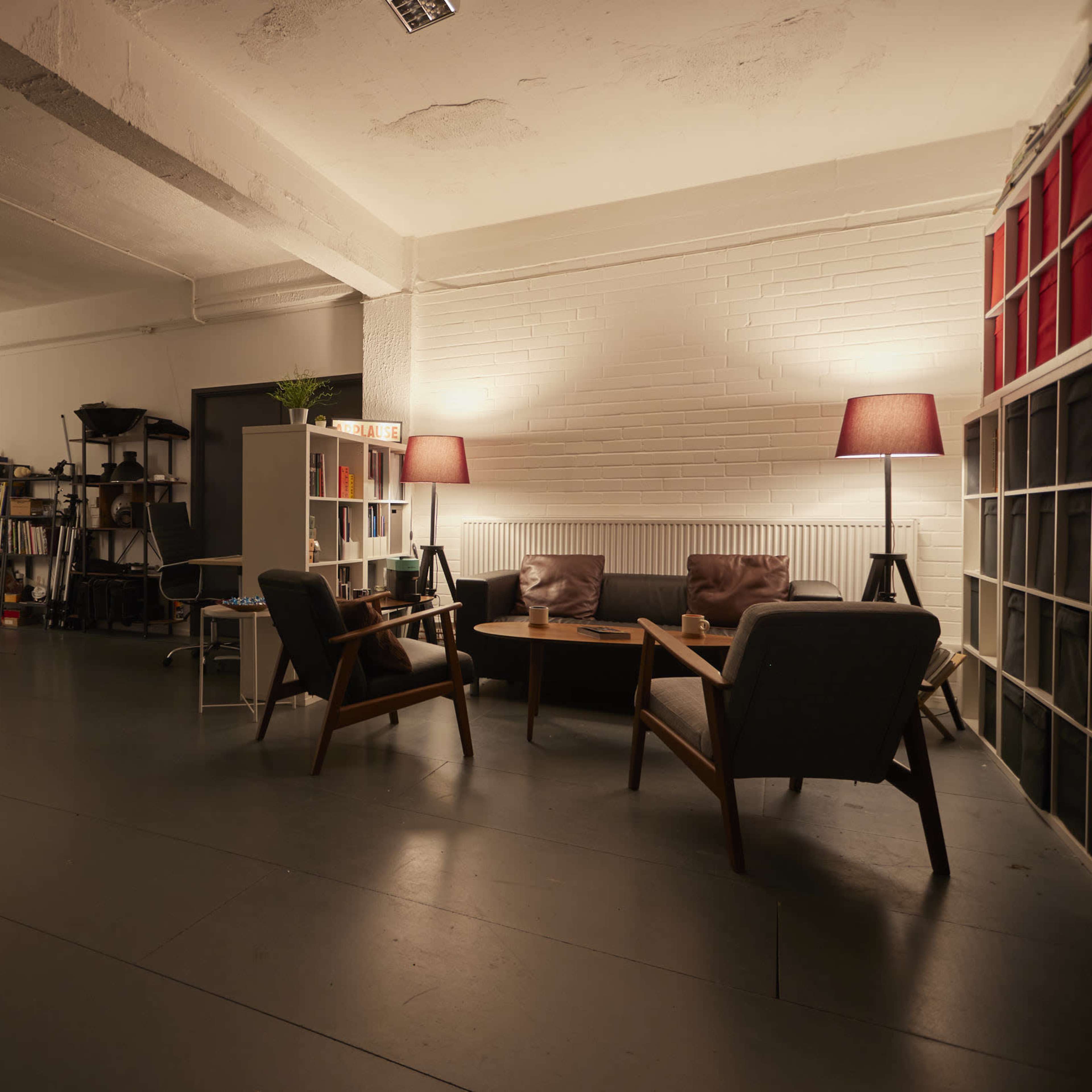 A spacious studio with wooden furniture, bookshelves, lamps, and a photography backdrop setup.