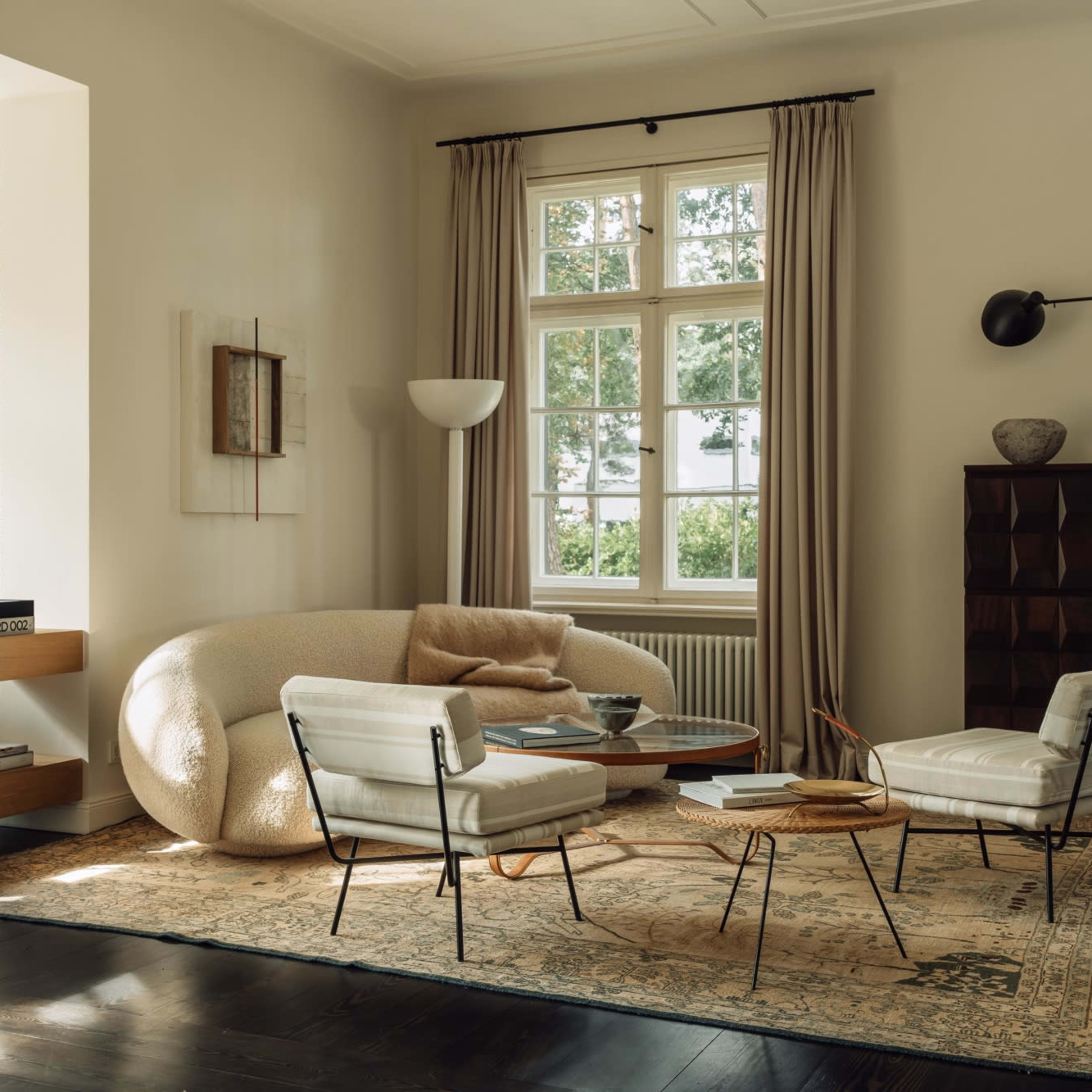 A modern living room with a curved sofa, two armchairs, a coffee table, and large windows allowing natural light to enter.