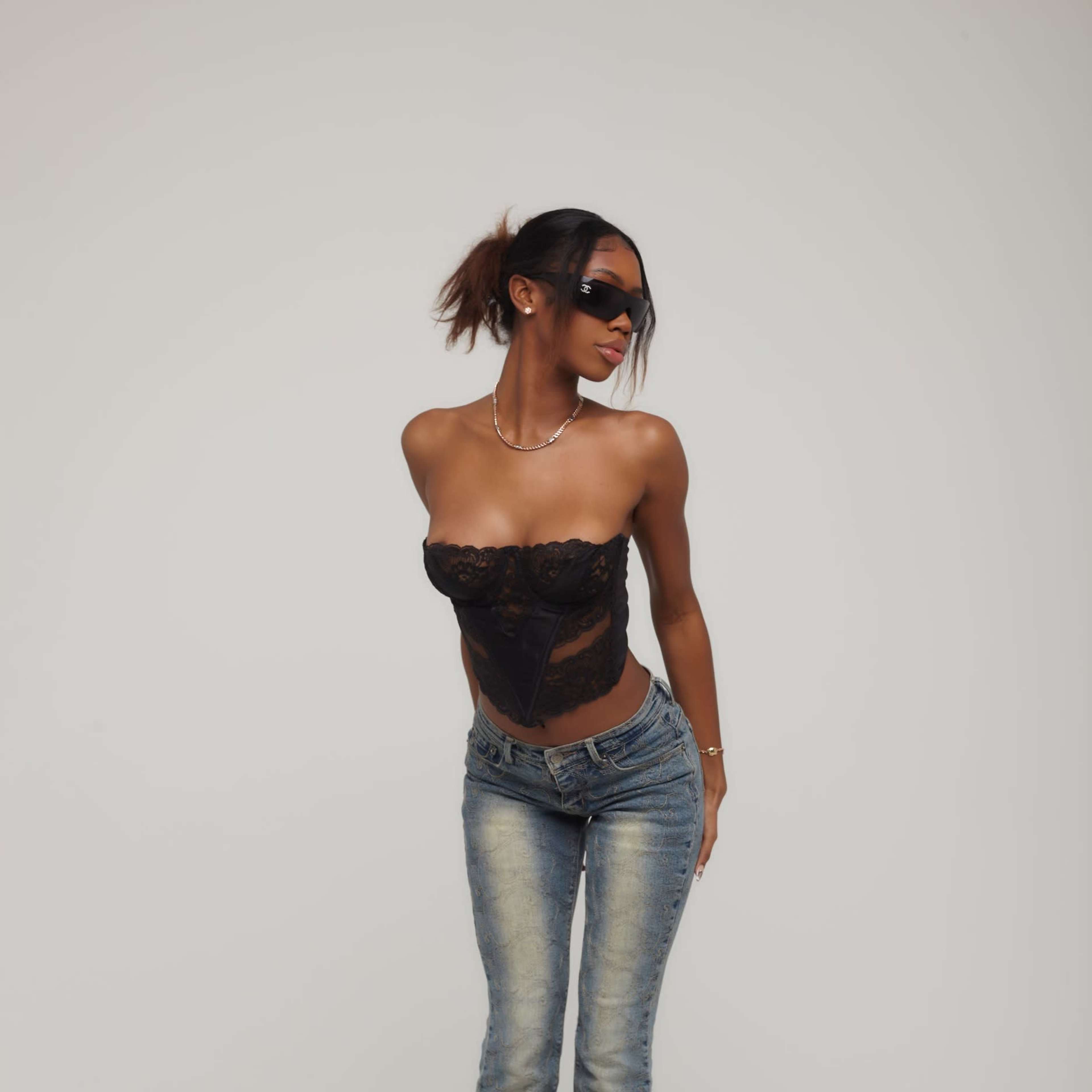 A woman in a black lace top and flared jeans stands against a neutral background.