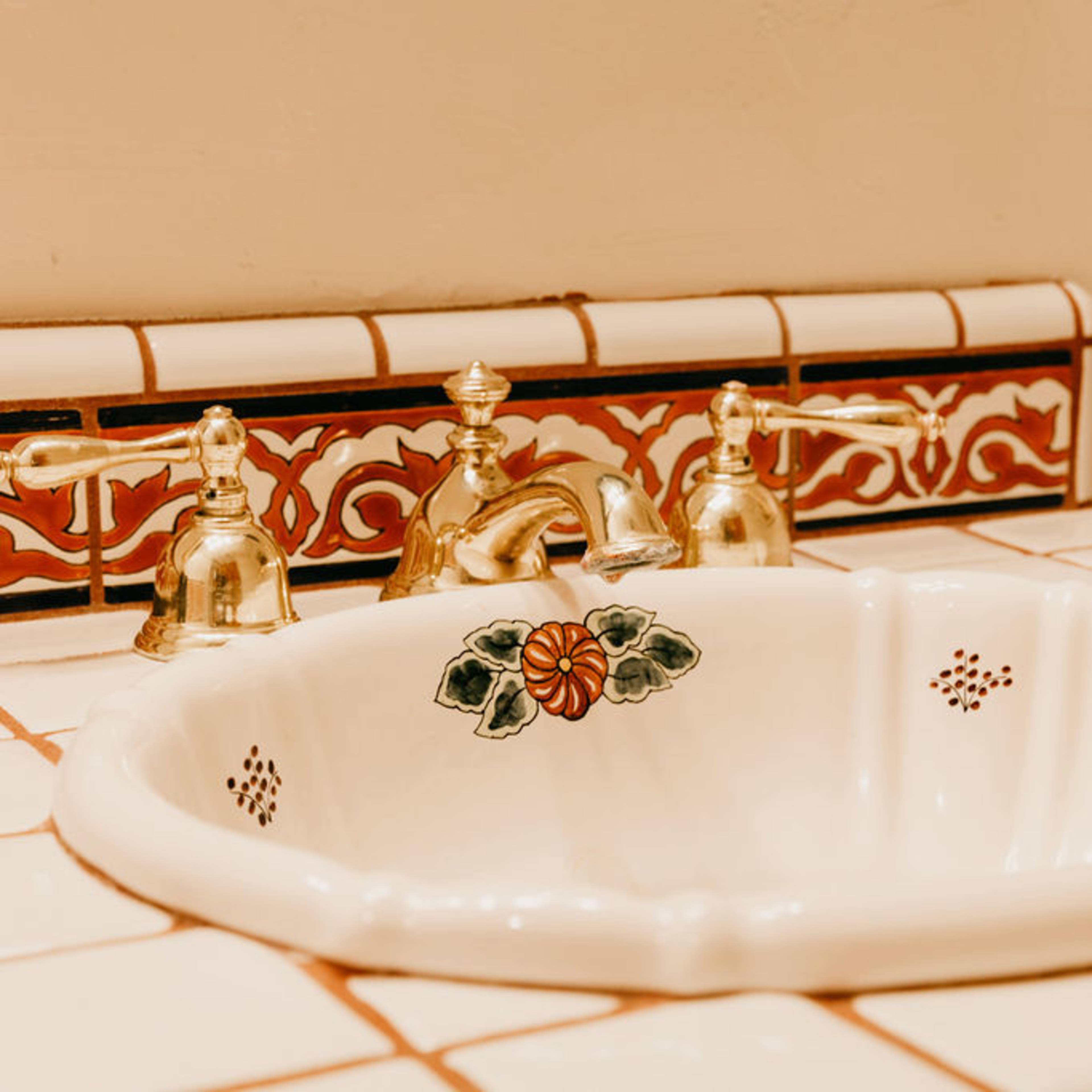 A decorative bathroom sink with a tiled countertop and faucets in a vintage style.