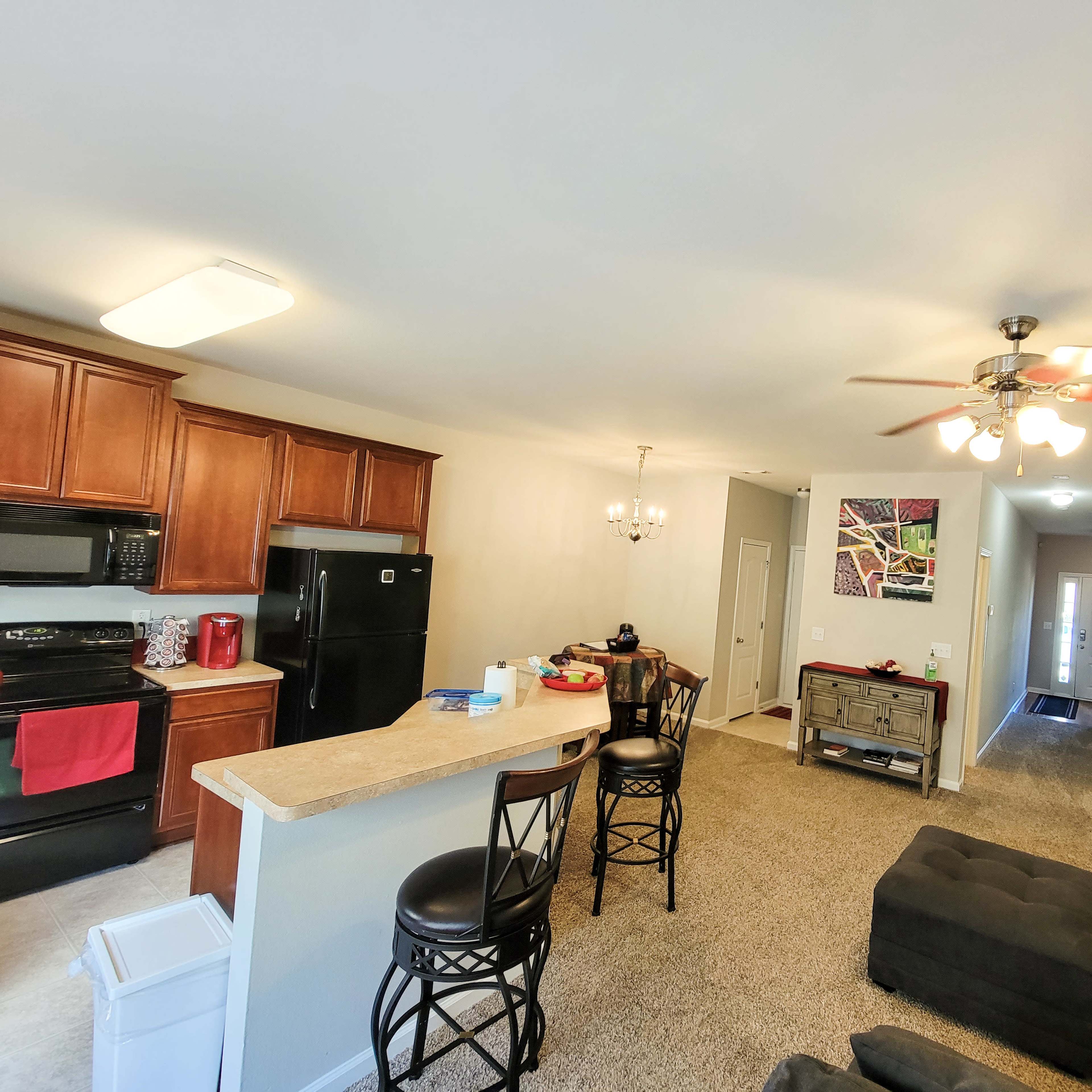 A modern apartment living space with a kitchen featuring dark wood cabinets, a black refrigerator, and a living area with a sectional sofa and a coffee table.
