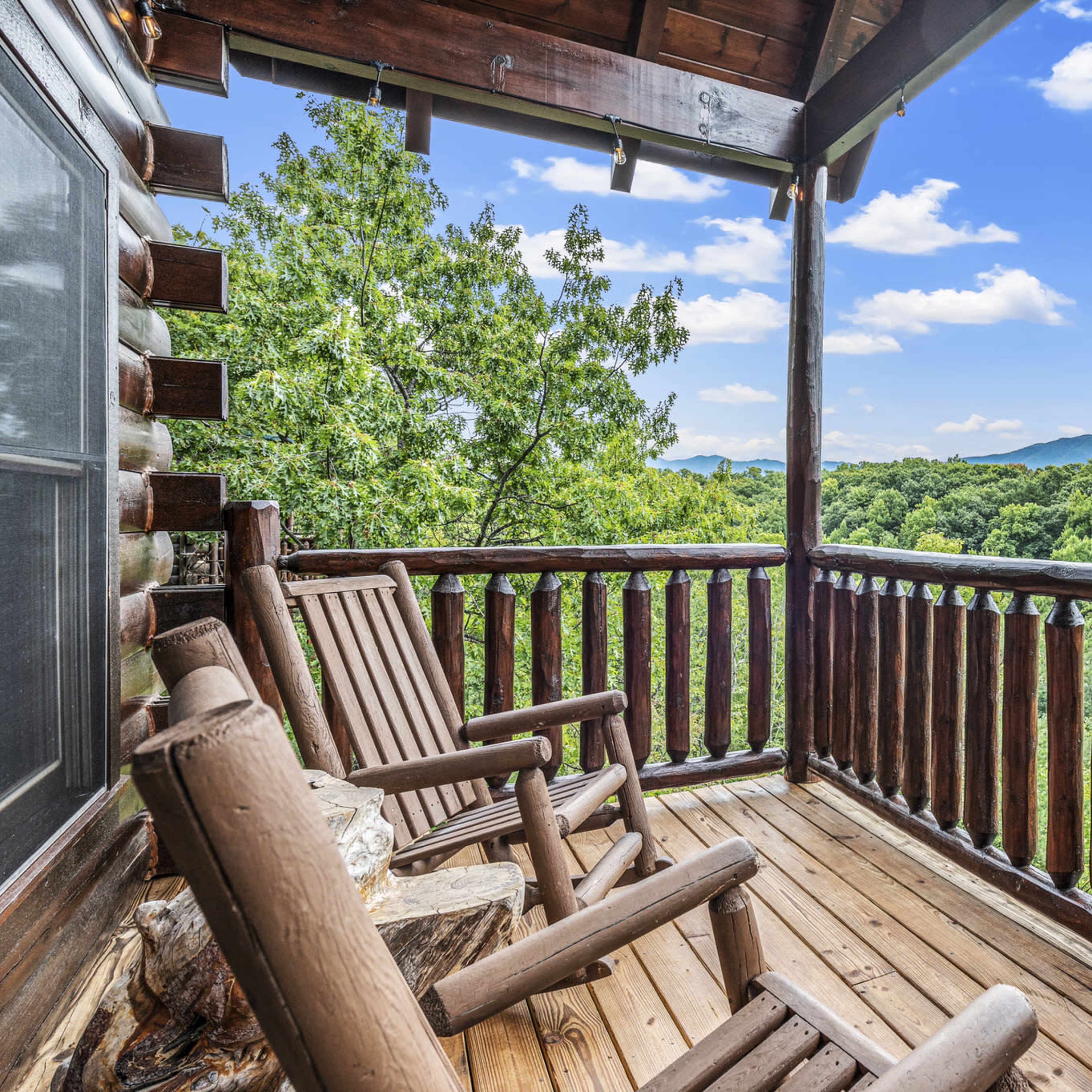 A wooden balcony features rocking chairs and overlooks a lush green landscape with distant mountains under a blue sky.