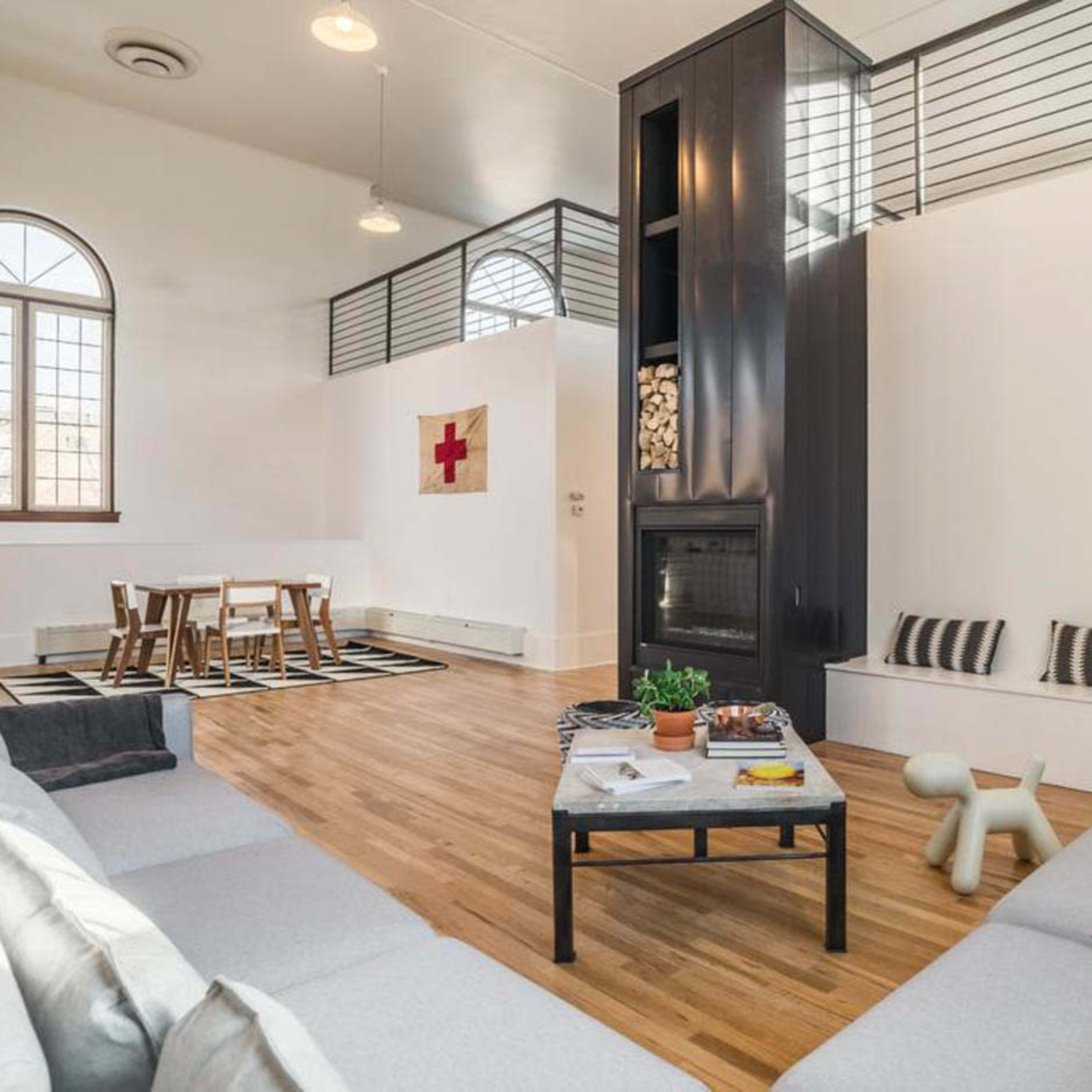 A spacious living room with modern furnishings, including a gray sectional sofa, a wooden dining table, and a central fireplace.