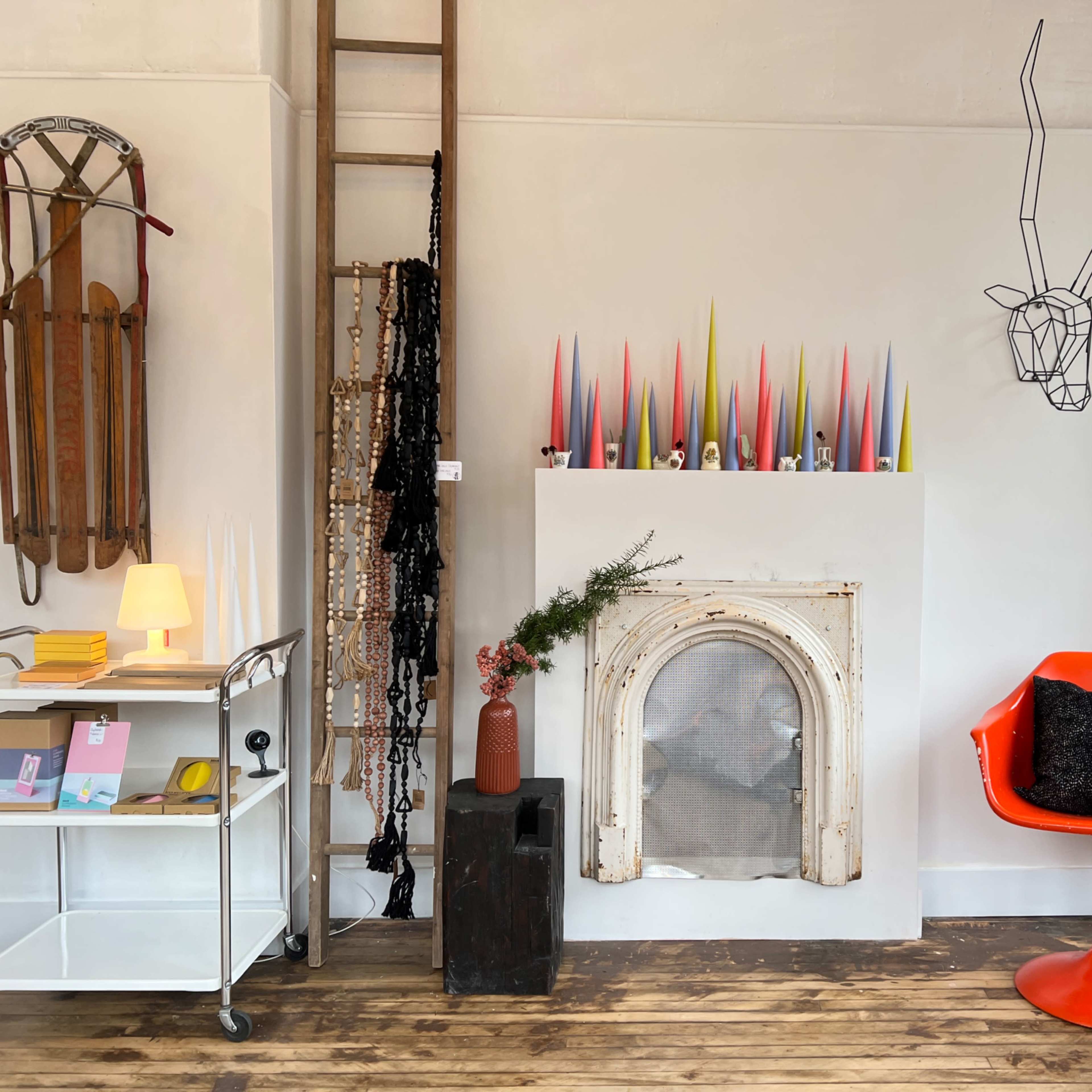 A cozy interior featuring a white wall with colorful candles above a decorative fireplace, an orange chair, and various decorative items scattered around.