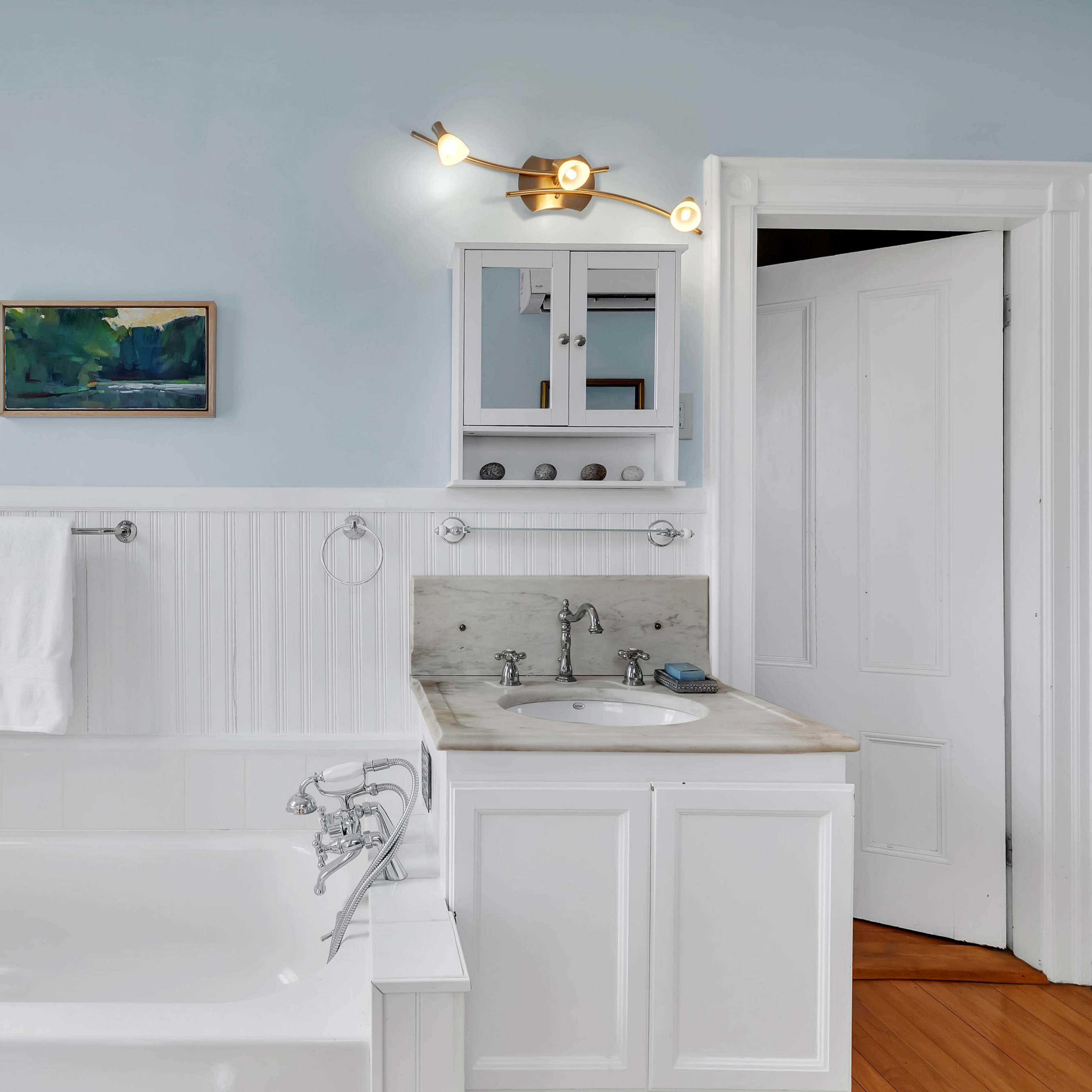 A clean bathroom features a white bathtub, a sink with a countertop, and a small mirror, all set against light blue walls.