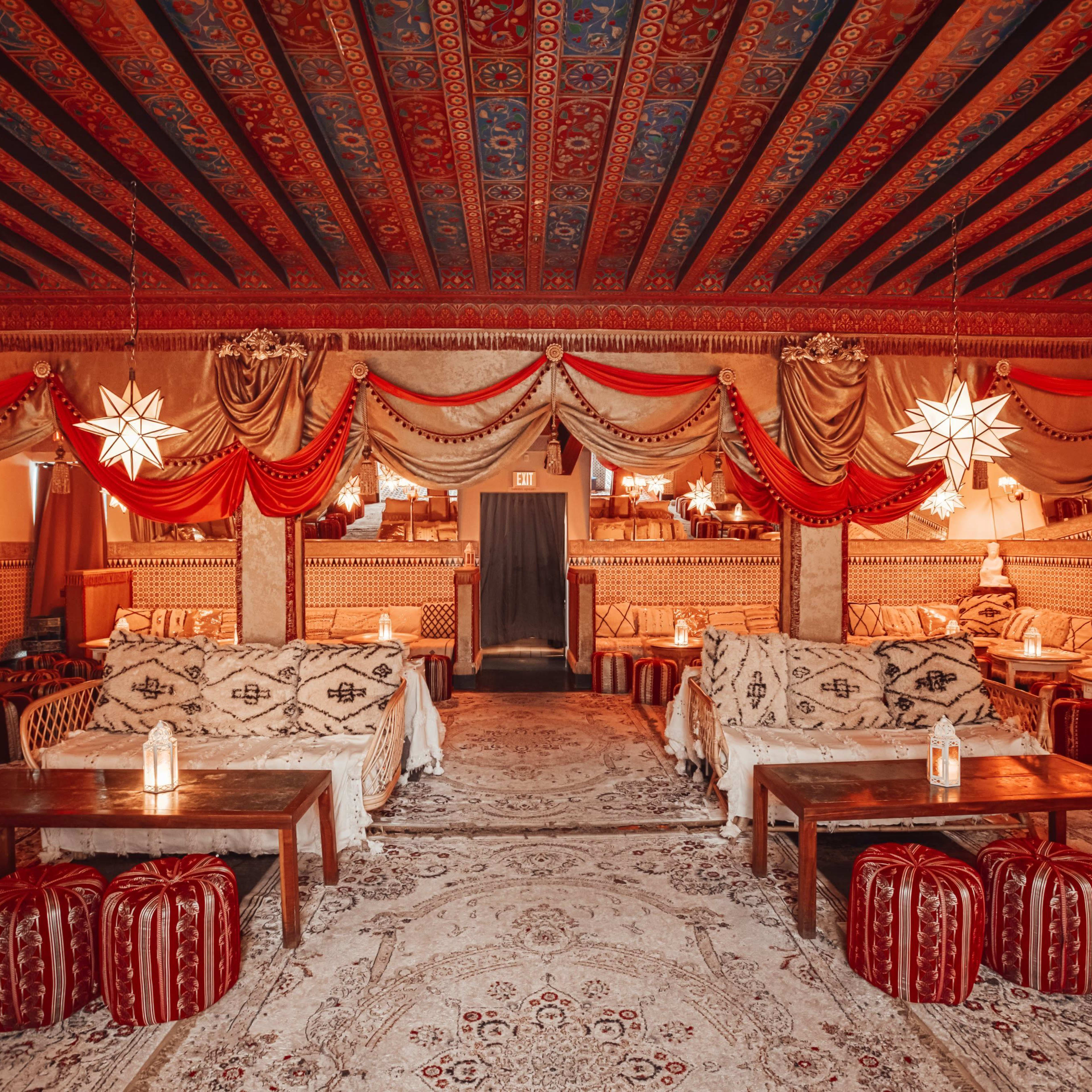 A lavishly decorated interior with intricately patterned ceilings, patterned carpets, plush seating areas, and lanterns illuminating the space.