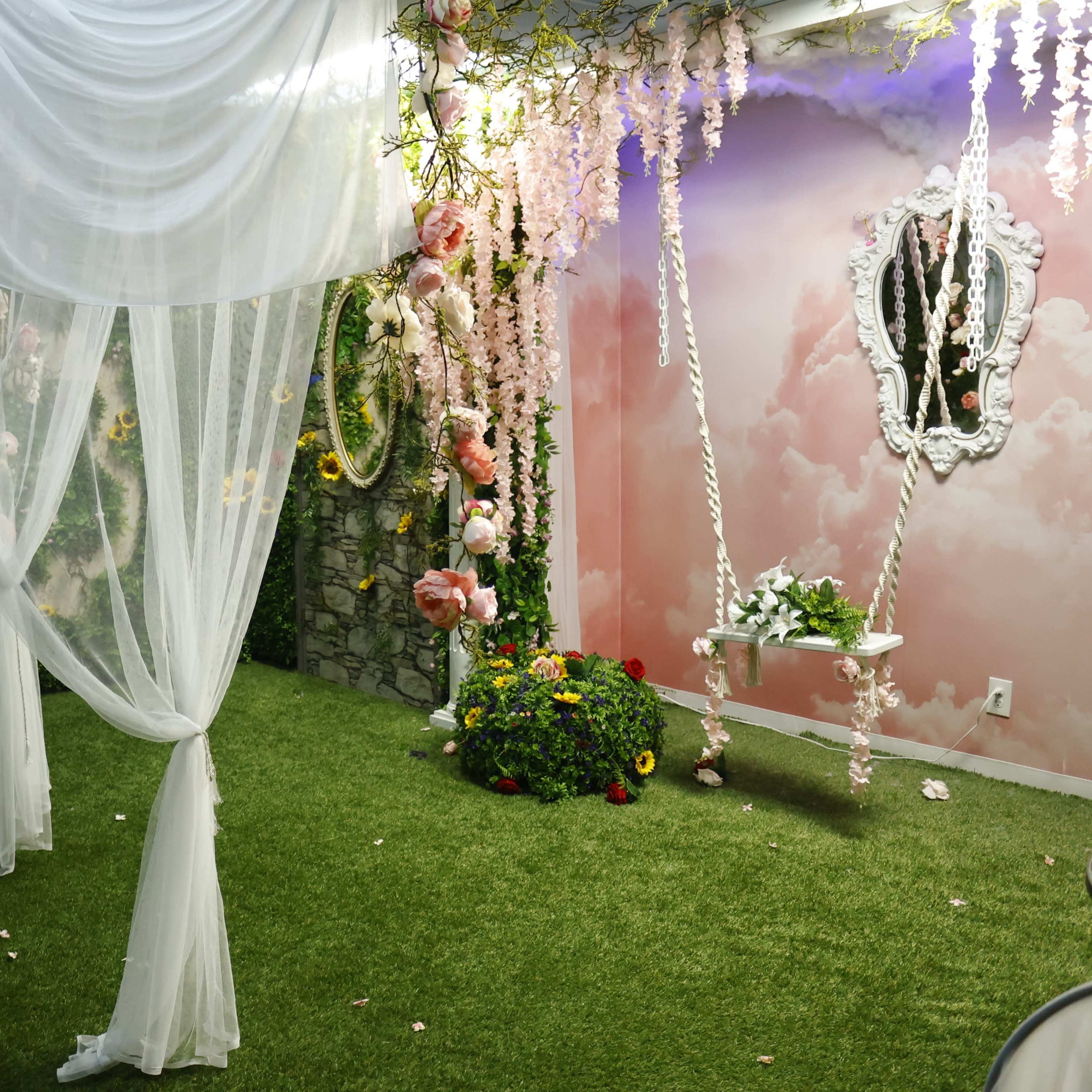 A decorative indoor space features sheer white drapery, artificial flowers, and a grassy floor.