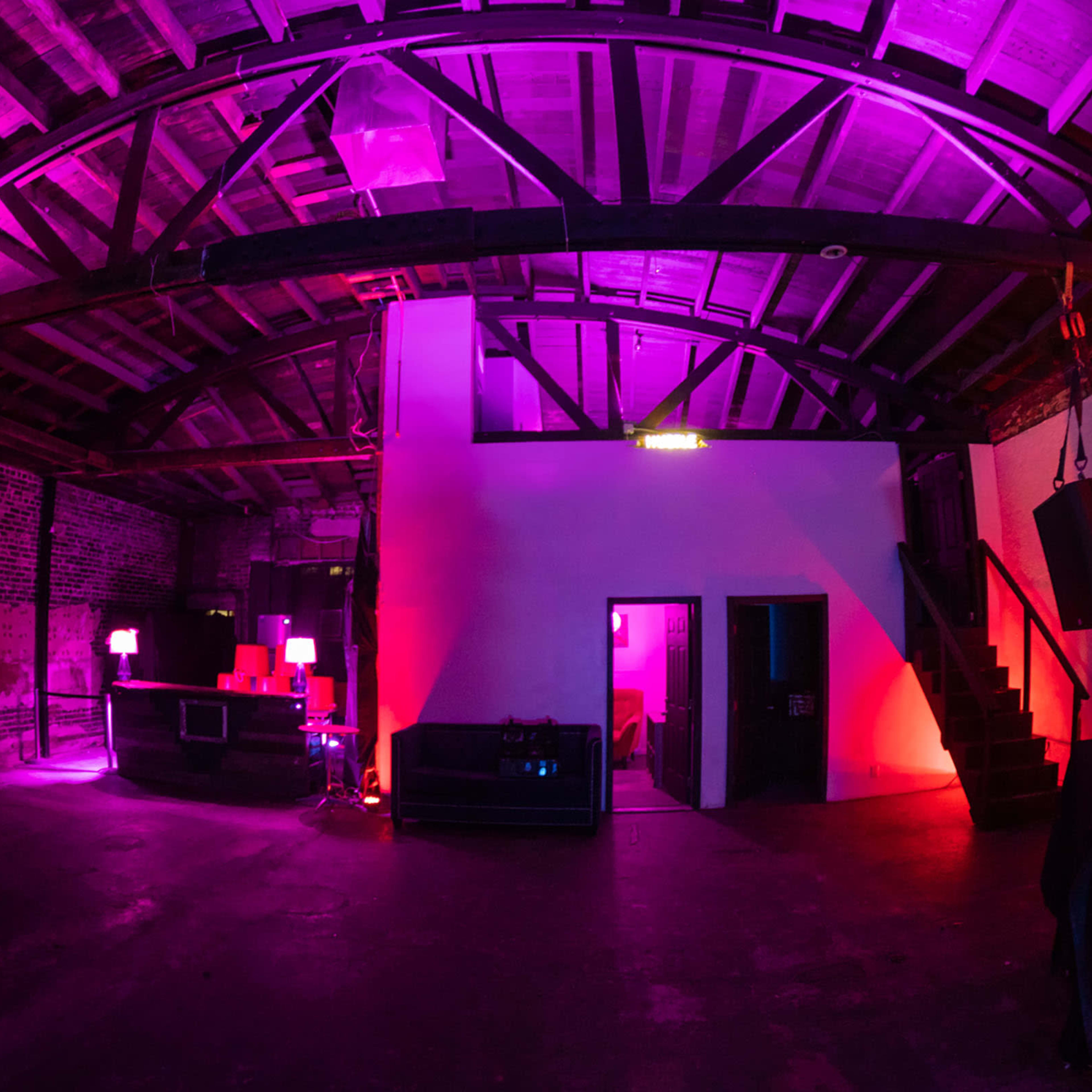 An industrial-style room with exposed brick walls and wooden beams, illuminated by purple and pink lighting.