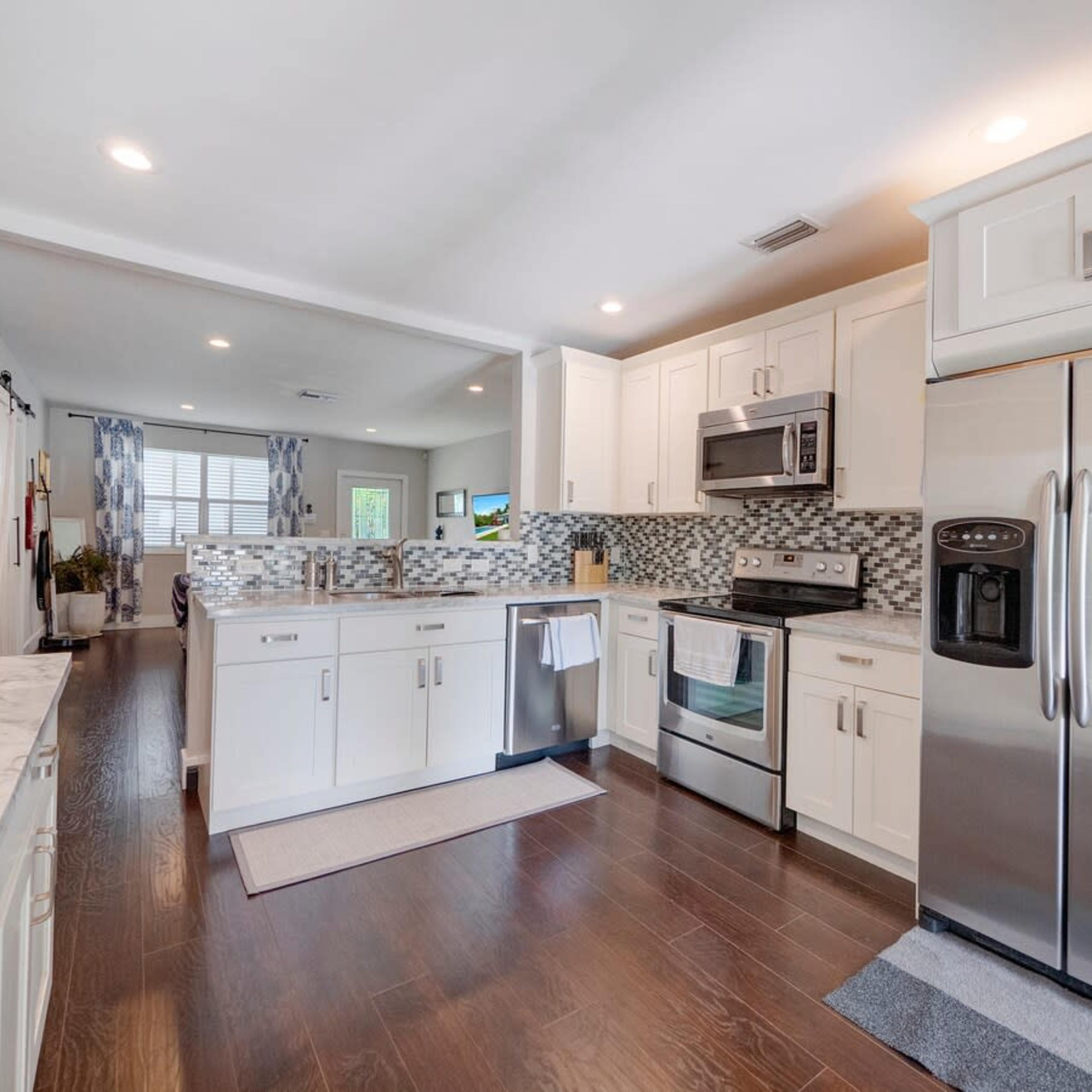 A modern kitchen with white cabinets, stainless steel appliances, and a tiled backsplash, featuring a view into an adjoining living space.